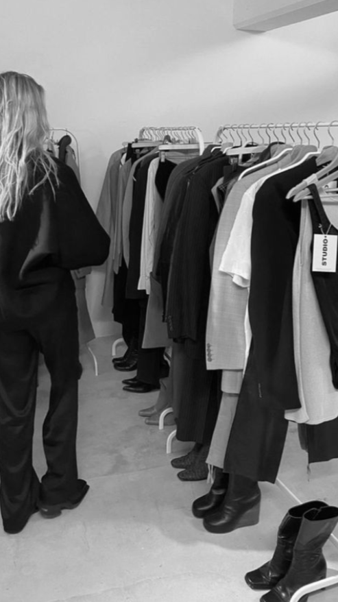 Person browsing clothing rack with various garments in an indoor setting.