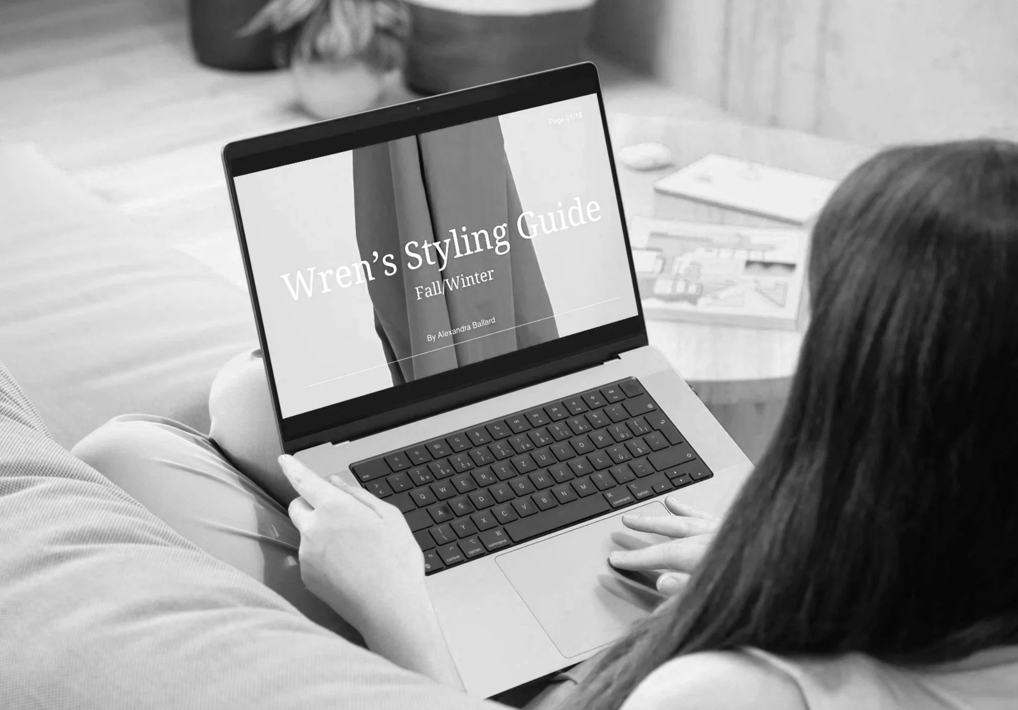 A person sitting on a couch using a laptop, which displays a digital magazine or document titled "Wren's Styling Guide Fall/Winter" by Alexandra Ballard, with books visible in the background.