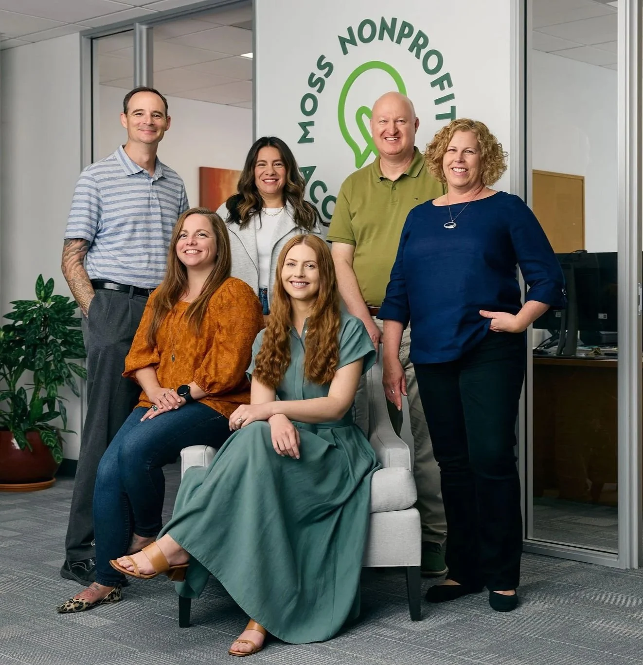The full Moss Nonprofit Accounting team posing together in front of their office logo wall in Walnut Creek, California