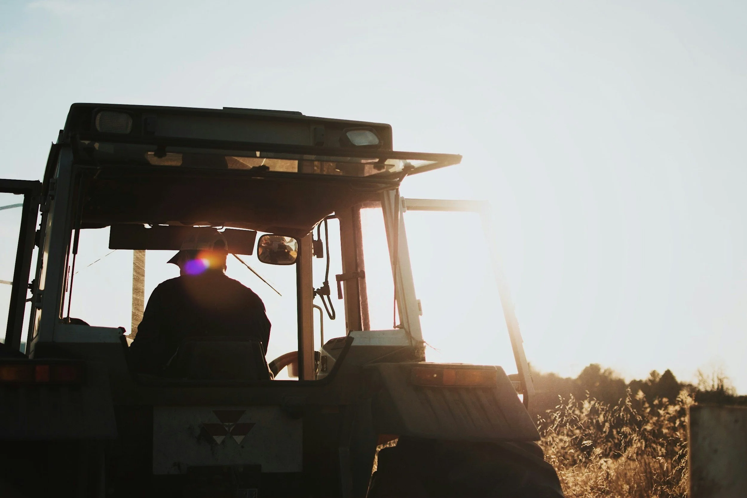 Farmer driving a tractor at sunset in a field.