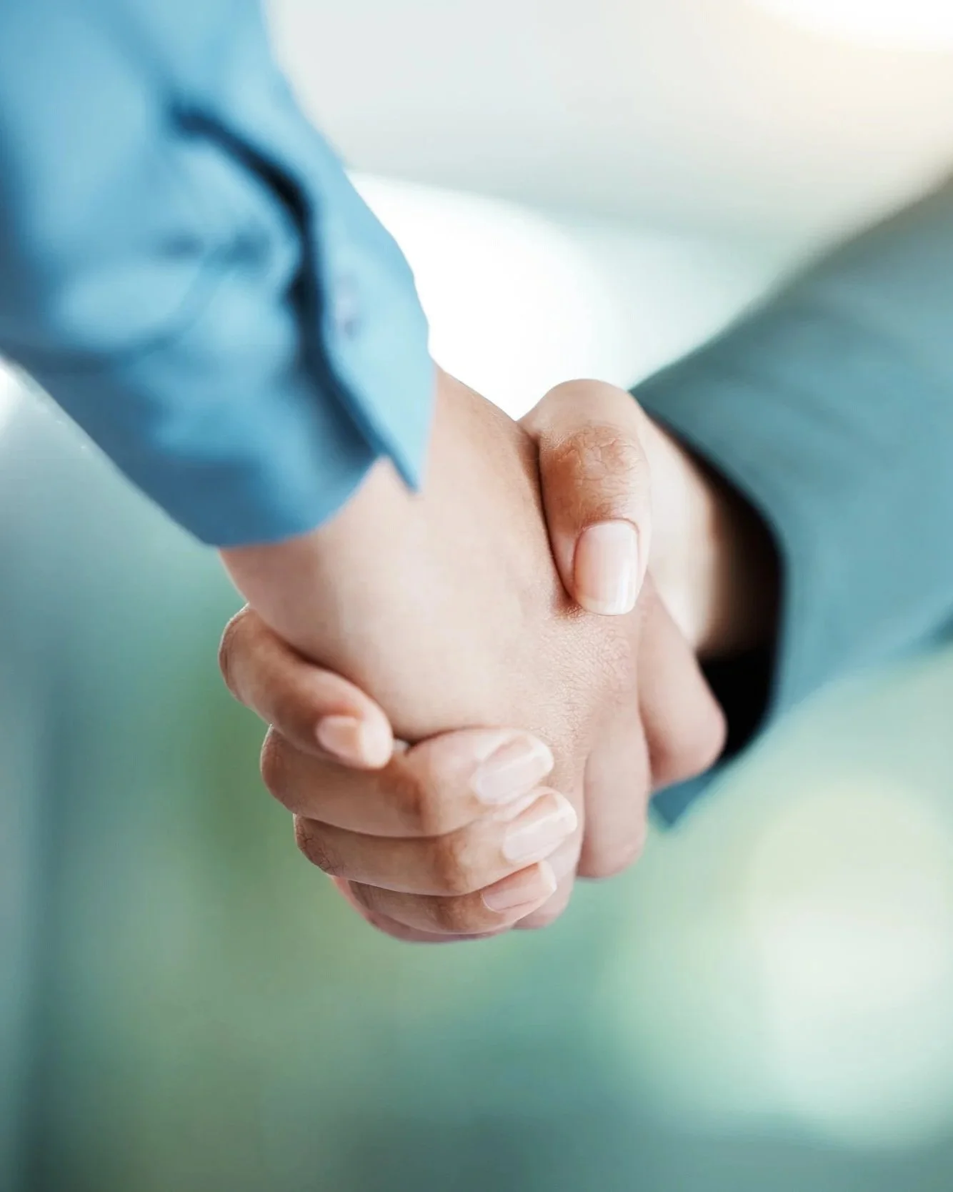 Close-up of two people shaking hands, one in a blue shirt and the other in formal attire.