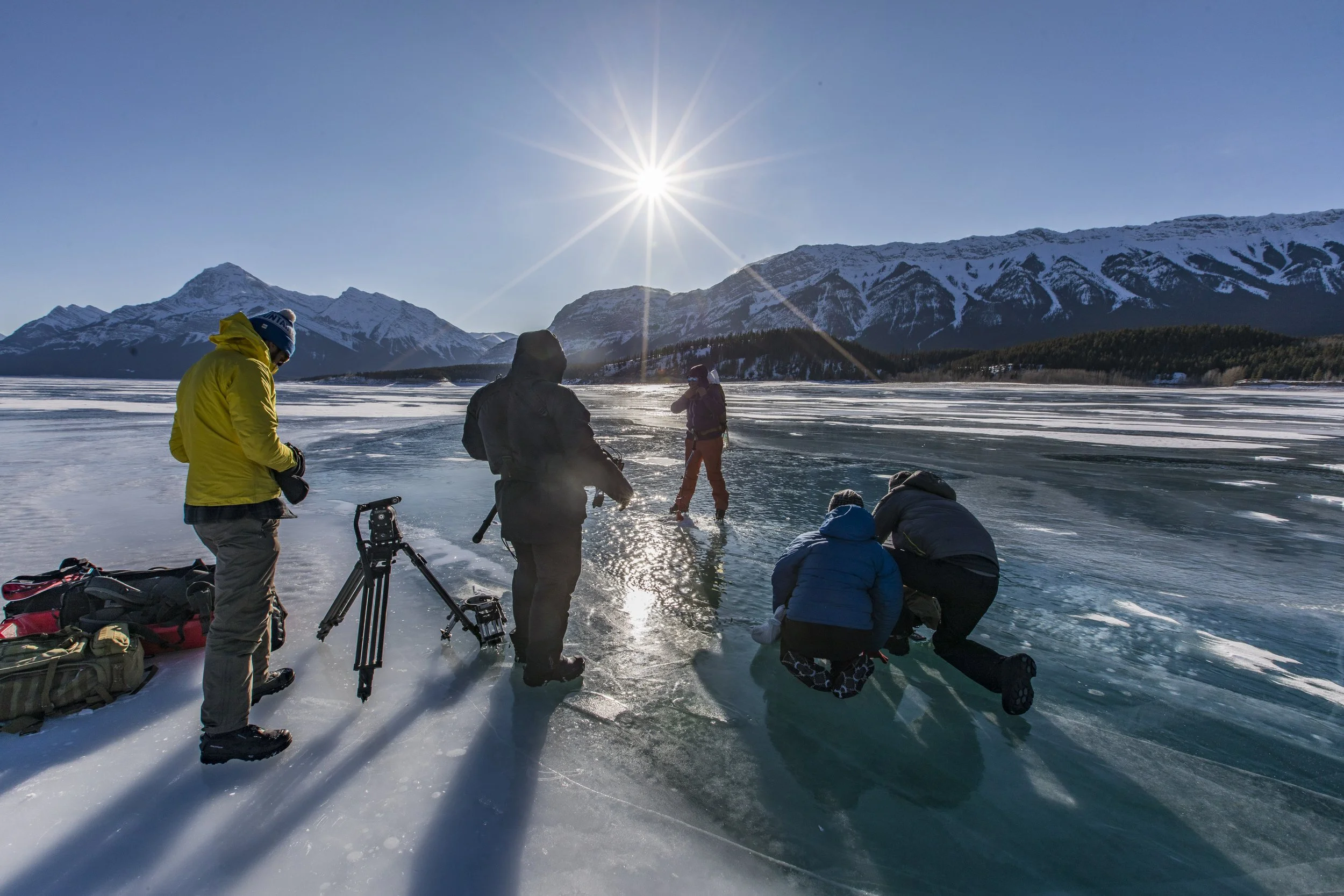 Film crew setting up to film a free diver going under the ice on a beautiful lake under sunny skies.