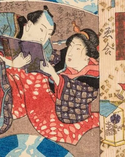 Two women in traditional Japanese kimonos look at a book together, sitting in an indoor setting with Japanese artwork and calligraphy on the wall behind them.