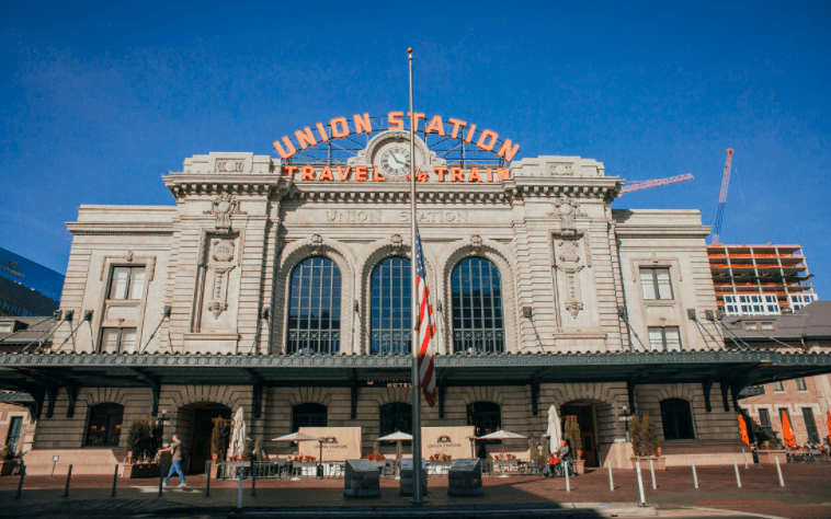 Front view of Union Station train station with a clock, American flag, and people walking outside on a sunny day.