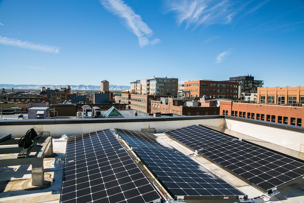 Solar panels installed on a rooftop with a cityscape and mountains in the background.