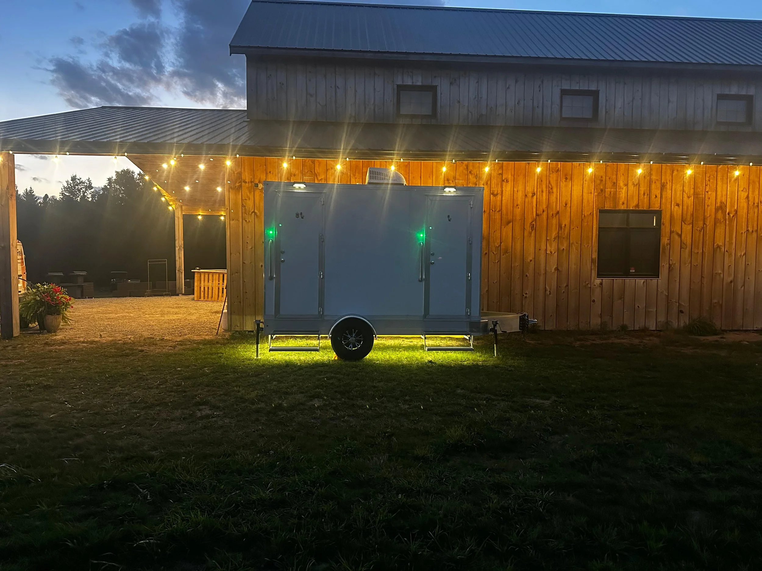 A white 2-unit washroom trailer parked outside a house.