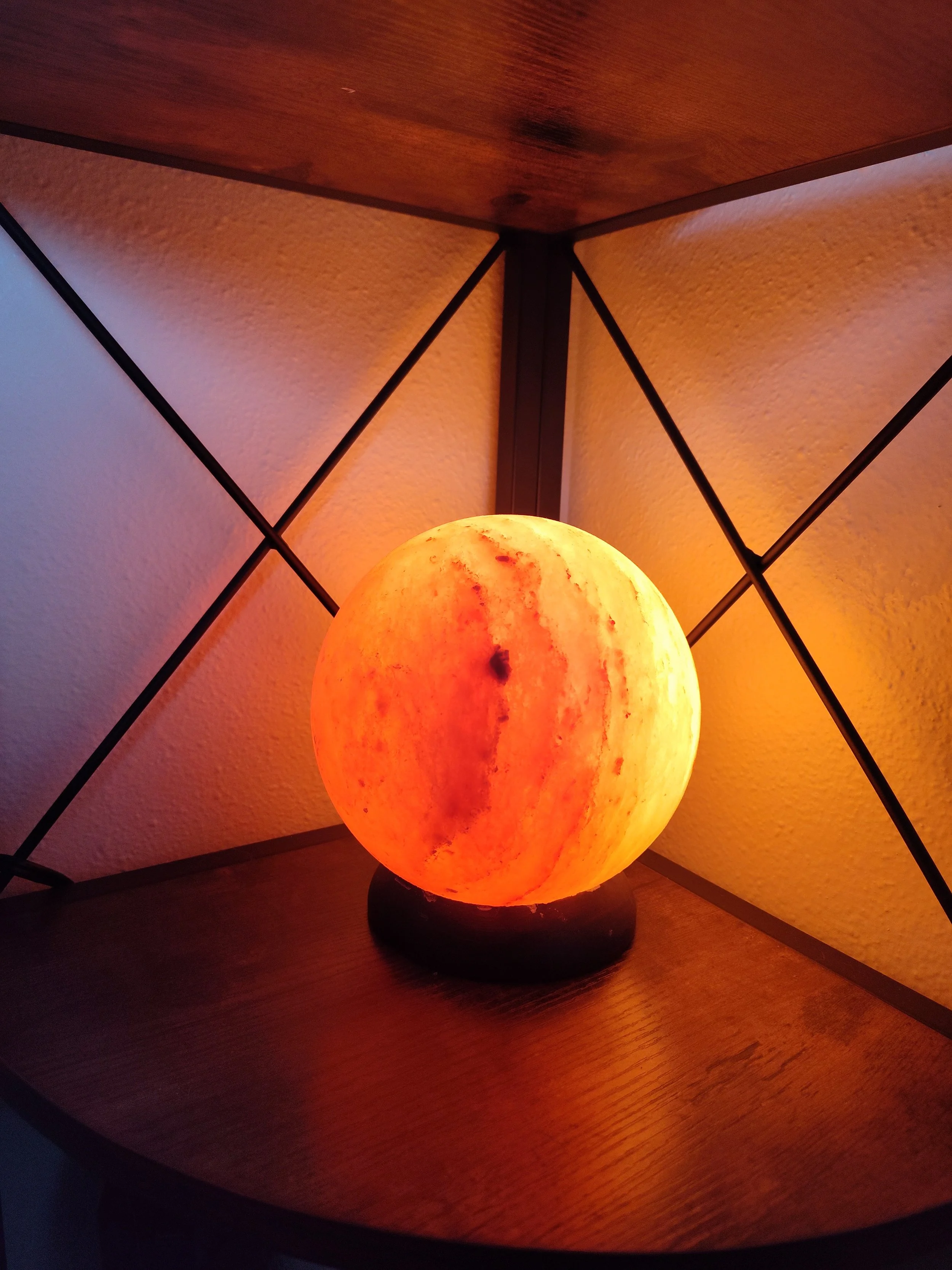 Himalayan salt lamp in the shape of the moon, glowing with orange light, placed on a wooden surface corner.