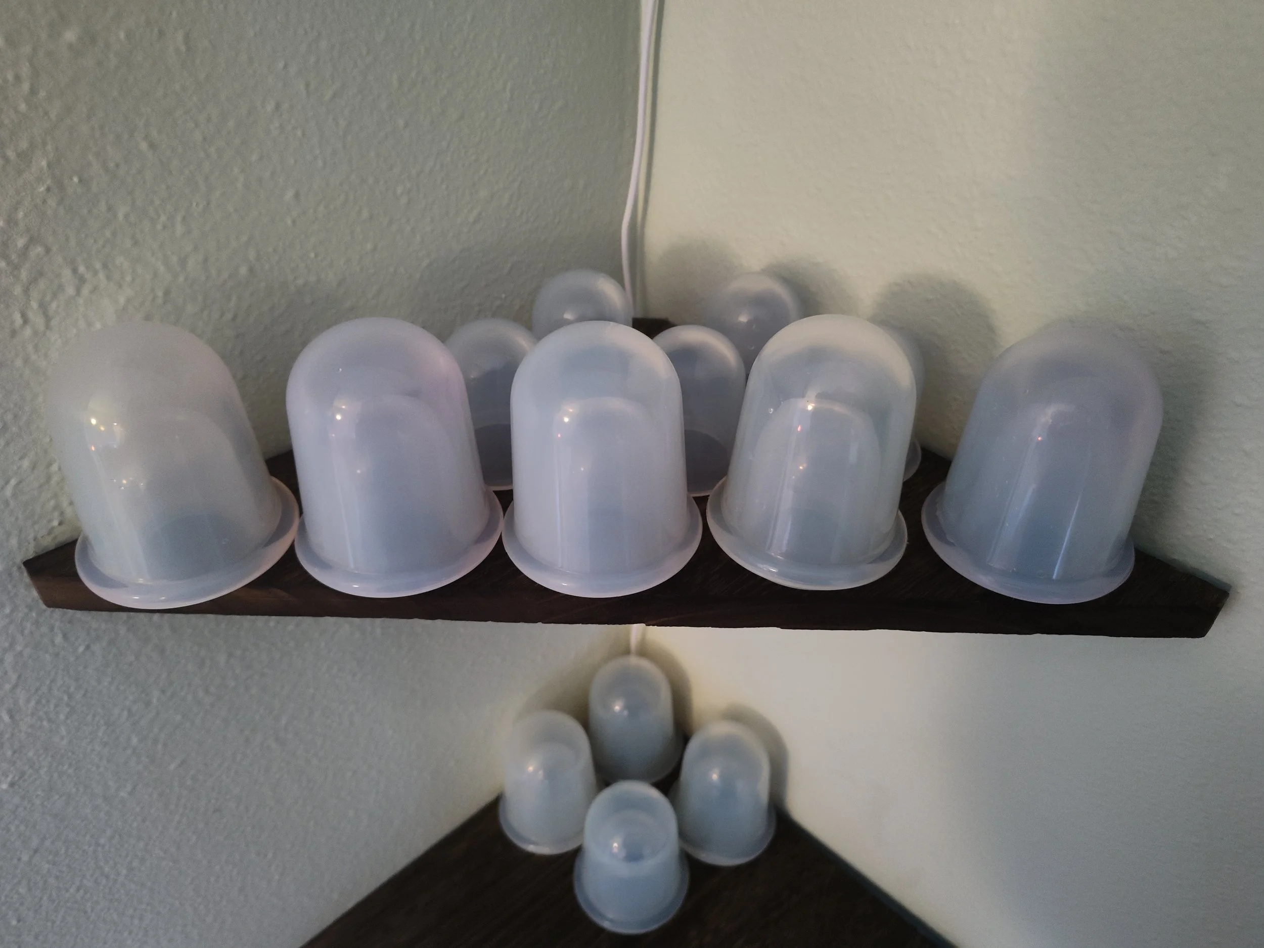 Several white plastic cups placed upside down on dark wooden shelves, with some on the shelves and others on the wall corner.