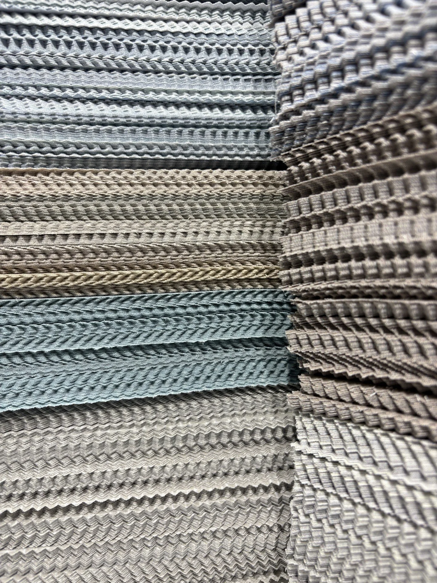 Stacked fabric swatches in various shades of gray, beige, and blue with different textures and patterns.