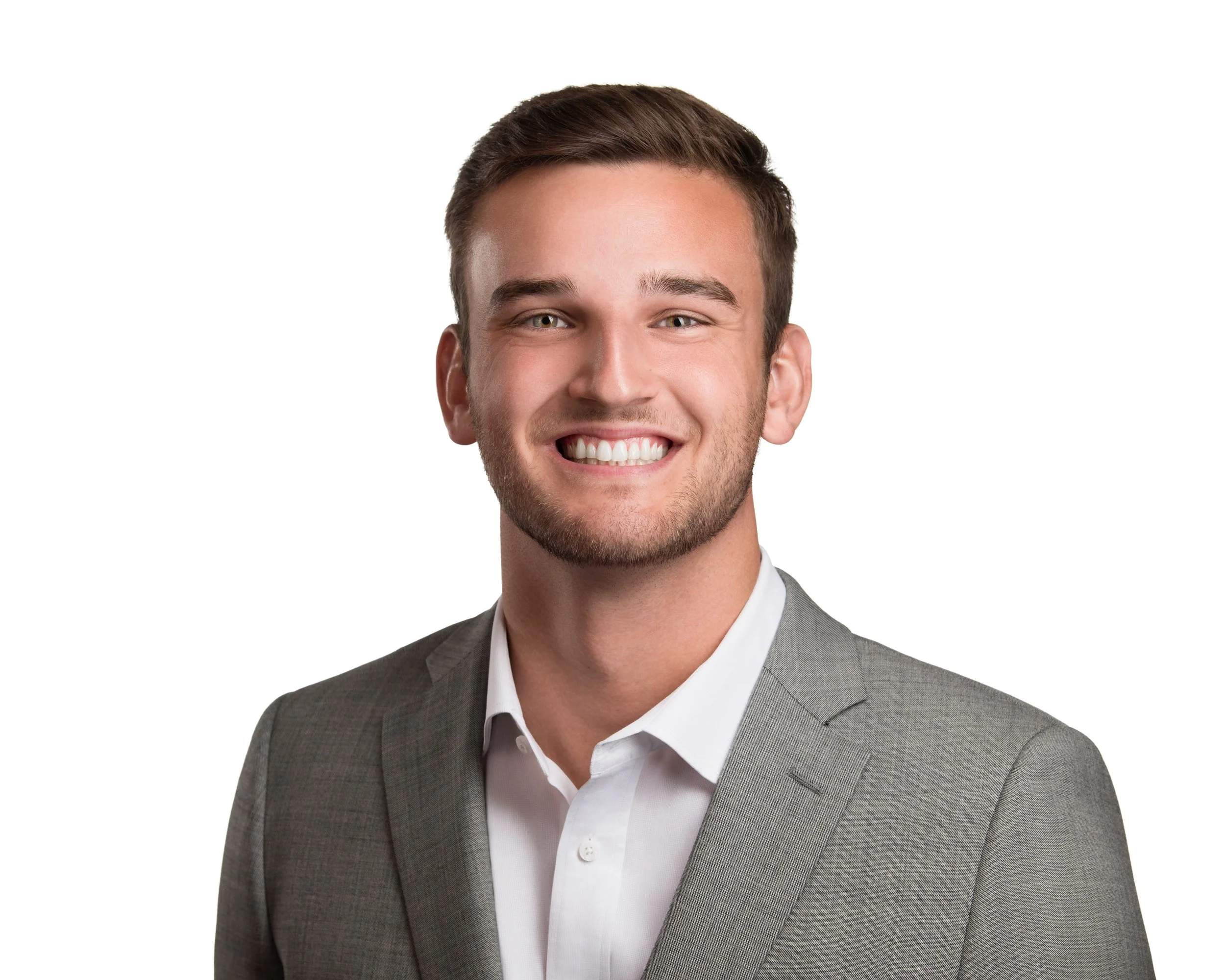 Young man with short brown hair, wearing a gray suit and white shirt, smiling against a white background.