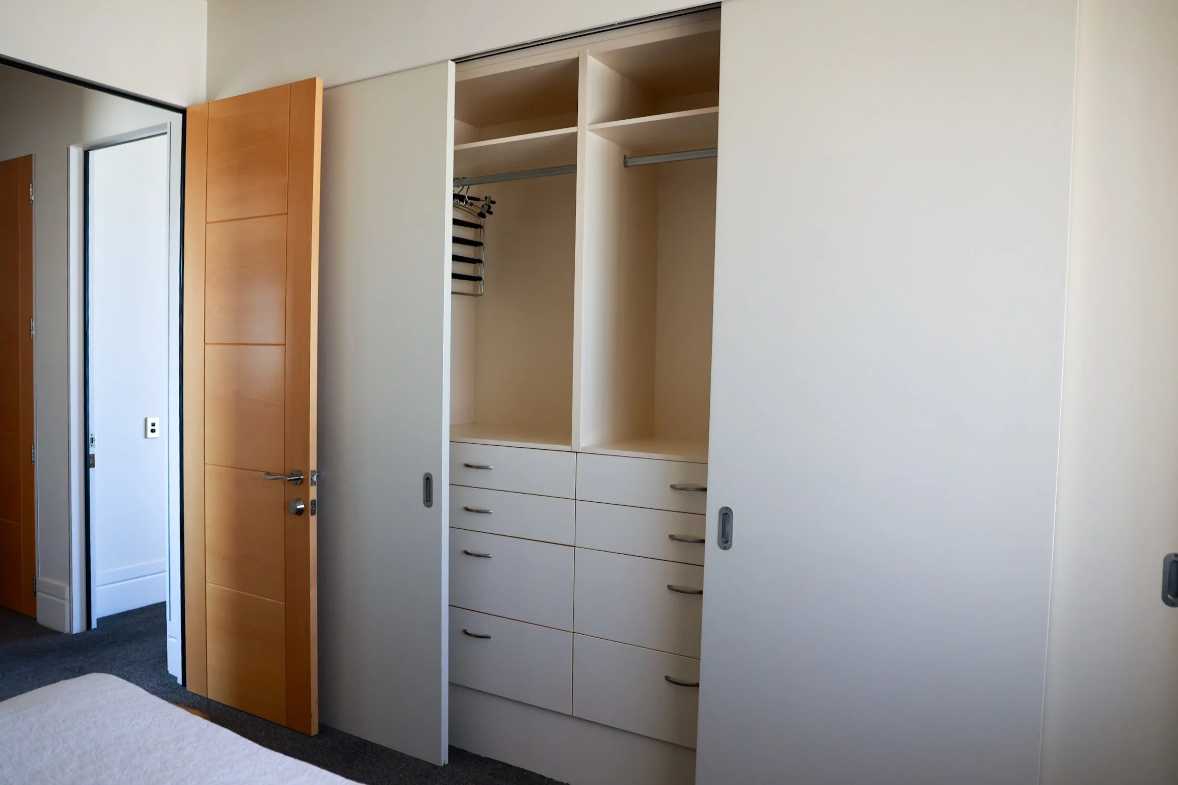 Empty bedroom closet with sliding doors, one partially open revealing shelves, drawers, and a hanging rod, in a modern bedroom.