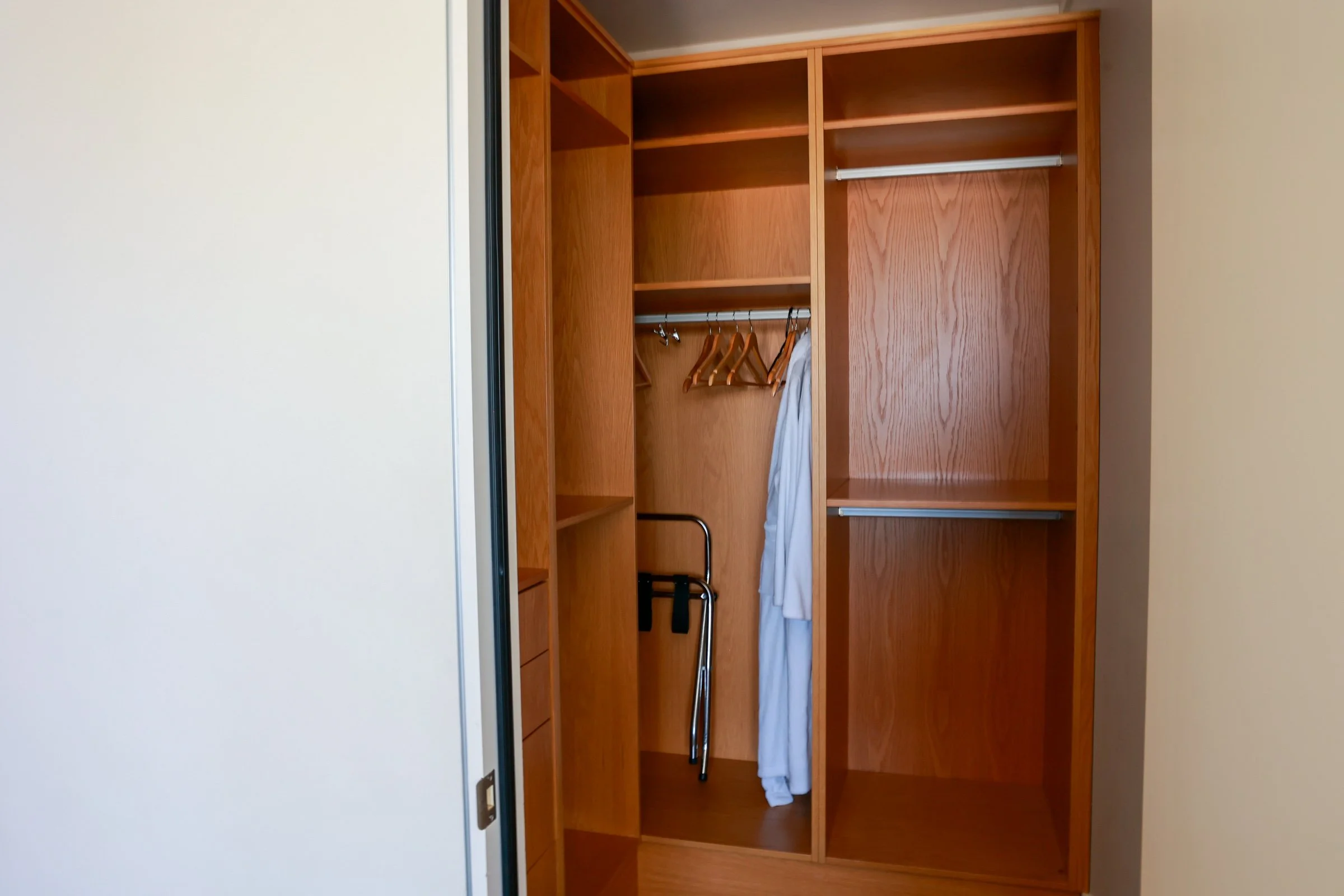Empty wooden closet with hanging space, shelves, and a white bathrobe.