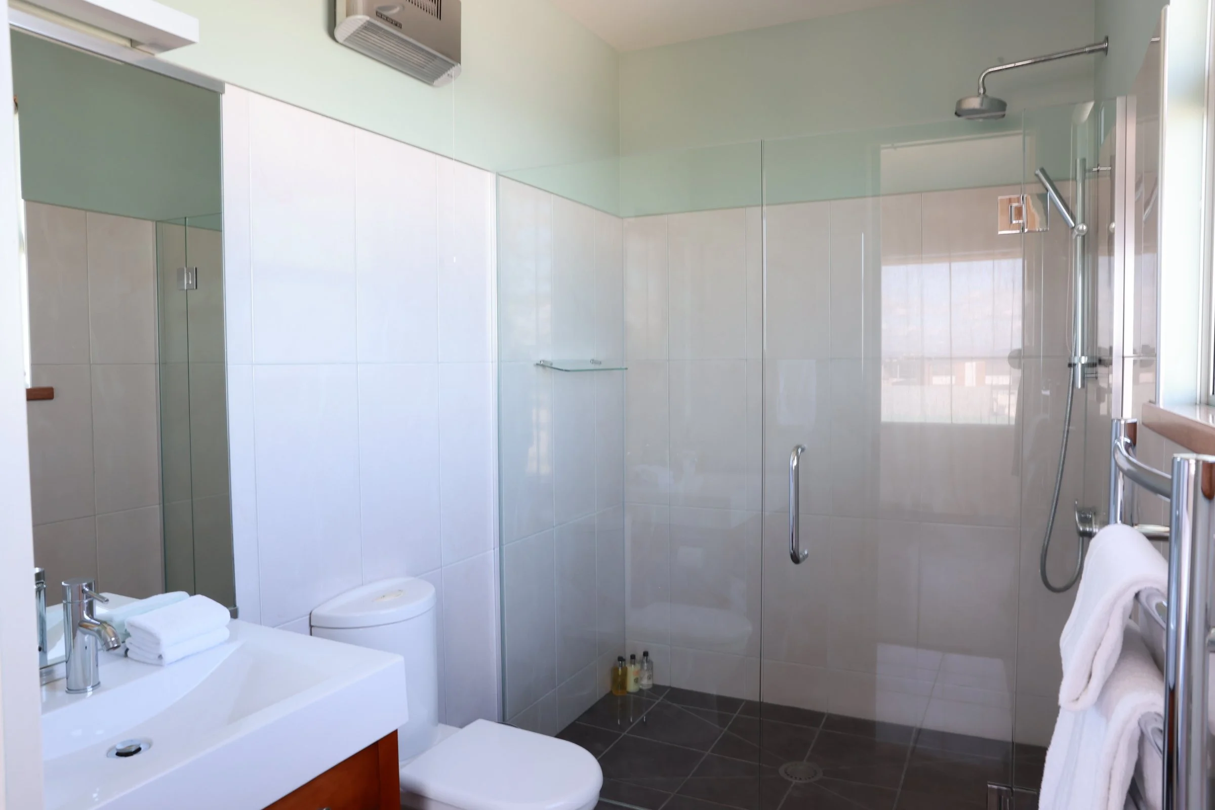 Modern bathroom with walk-in shower, glass door, white tiled walls, and a window, with towels on a rack.