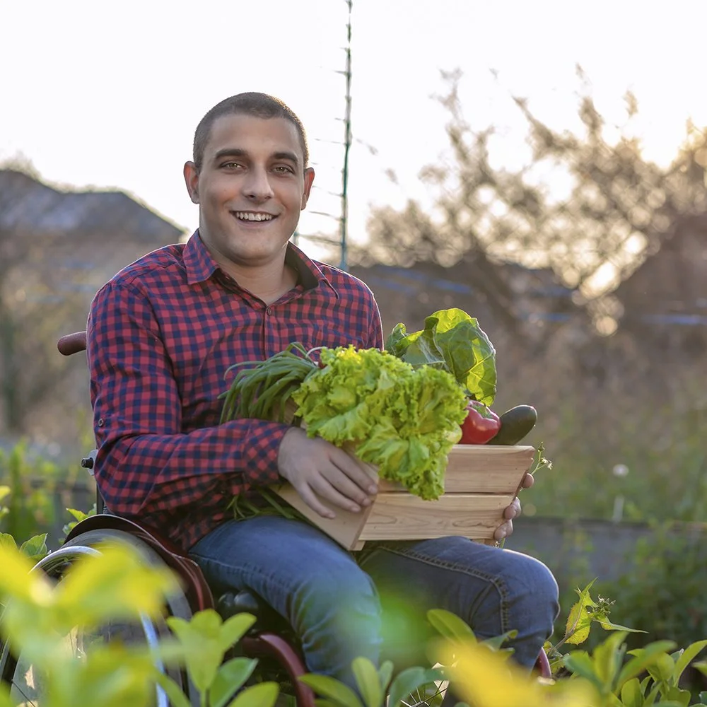 Special needs man in wheelchair holding box of vegetables from a garden