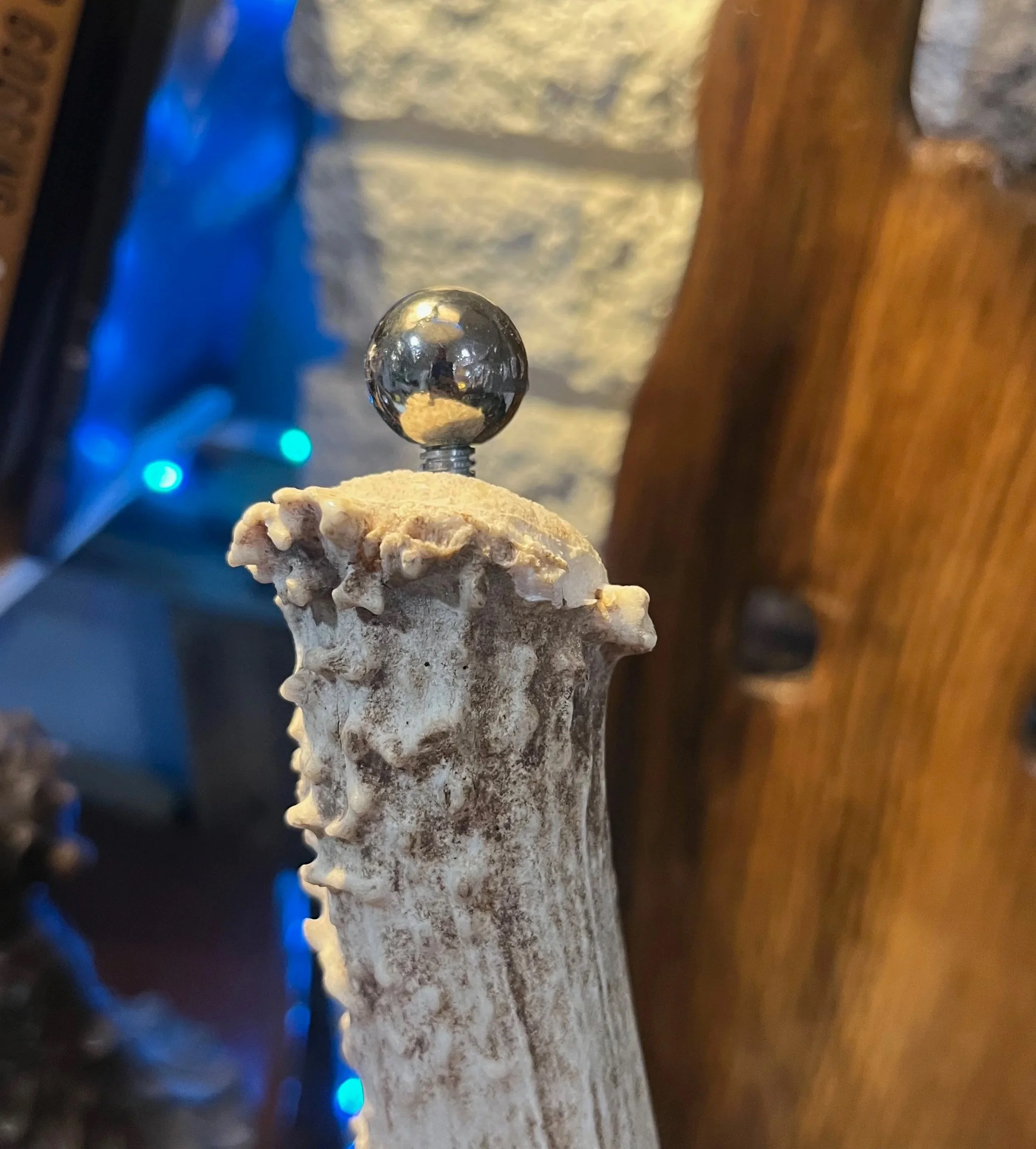 Close-up of a textured, weathered bone with a shiny metal ball on top, set against a background of a wooden surface and stone wall.