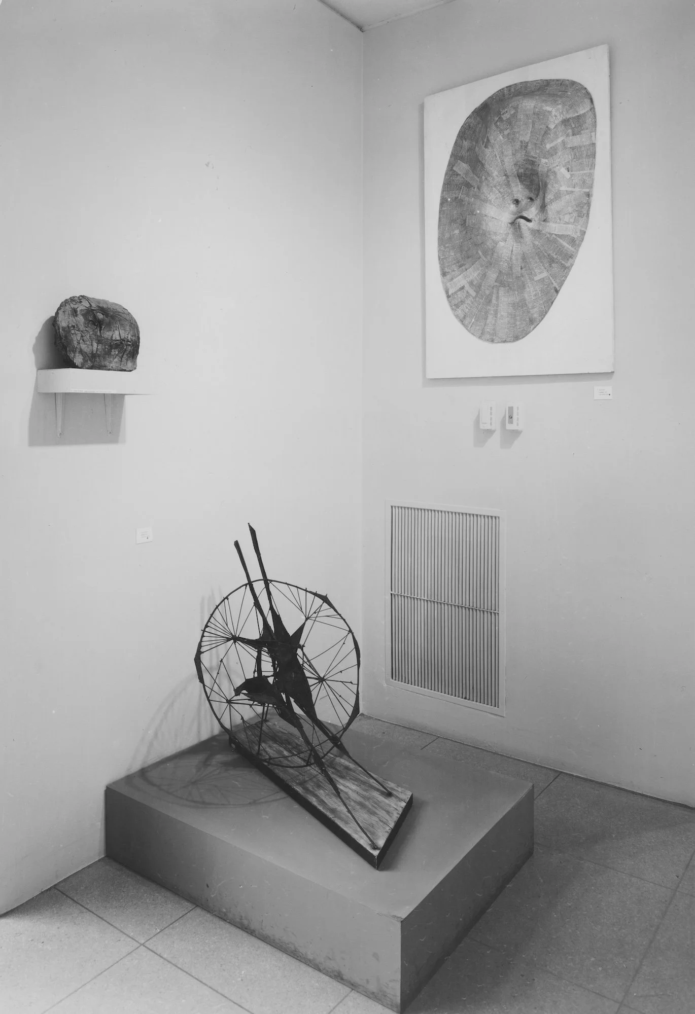 Art gallery with abstract sculptures and paintings, including a wooden sculpture on a pedestal, a wireframe sculpture on the floor, and paintings on the walls.