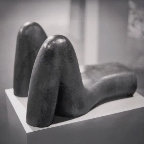 Black abstract sculpture resembling a reclining figure, displayed on a white pedestal.