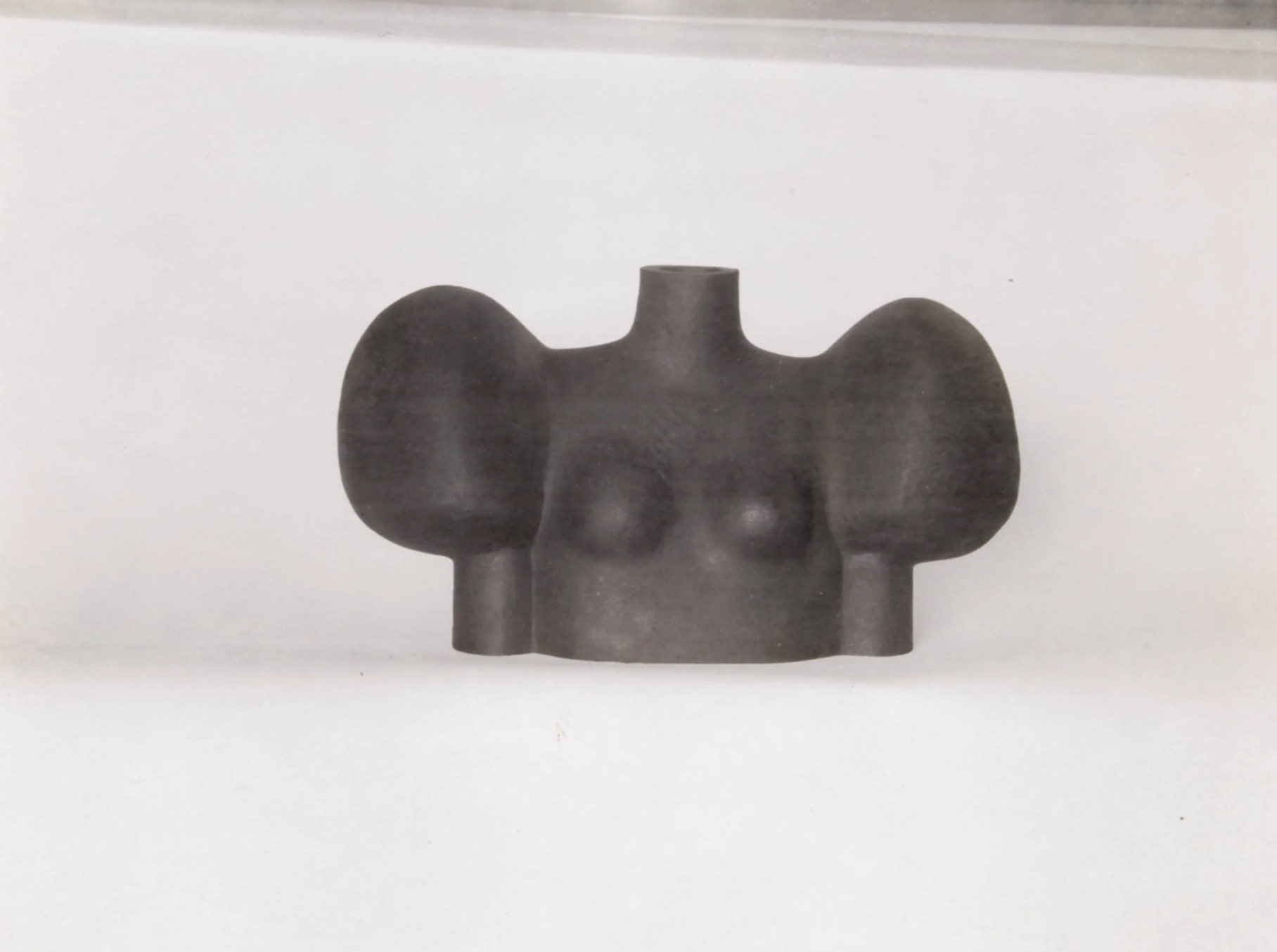 A sculpture of a person sitting in a chair, with the person's head resting on one hand. The sculpture appears to be made from various materials, with a patchwork design, and the chair has thin, metal legs.