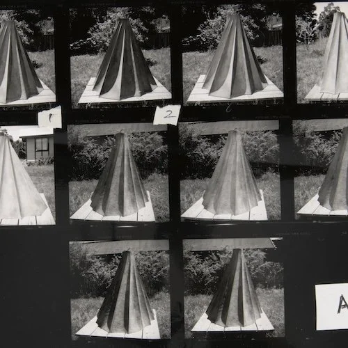 A contact sheet of black and white photographs showing a wooden outdoor table with a striped umbrella, taken from different angles and lighting conditions.
