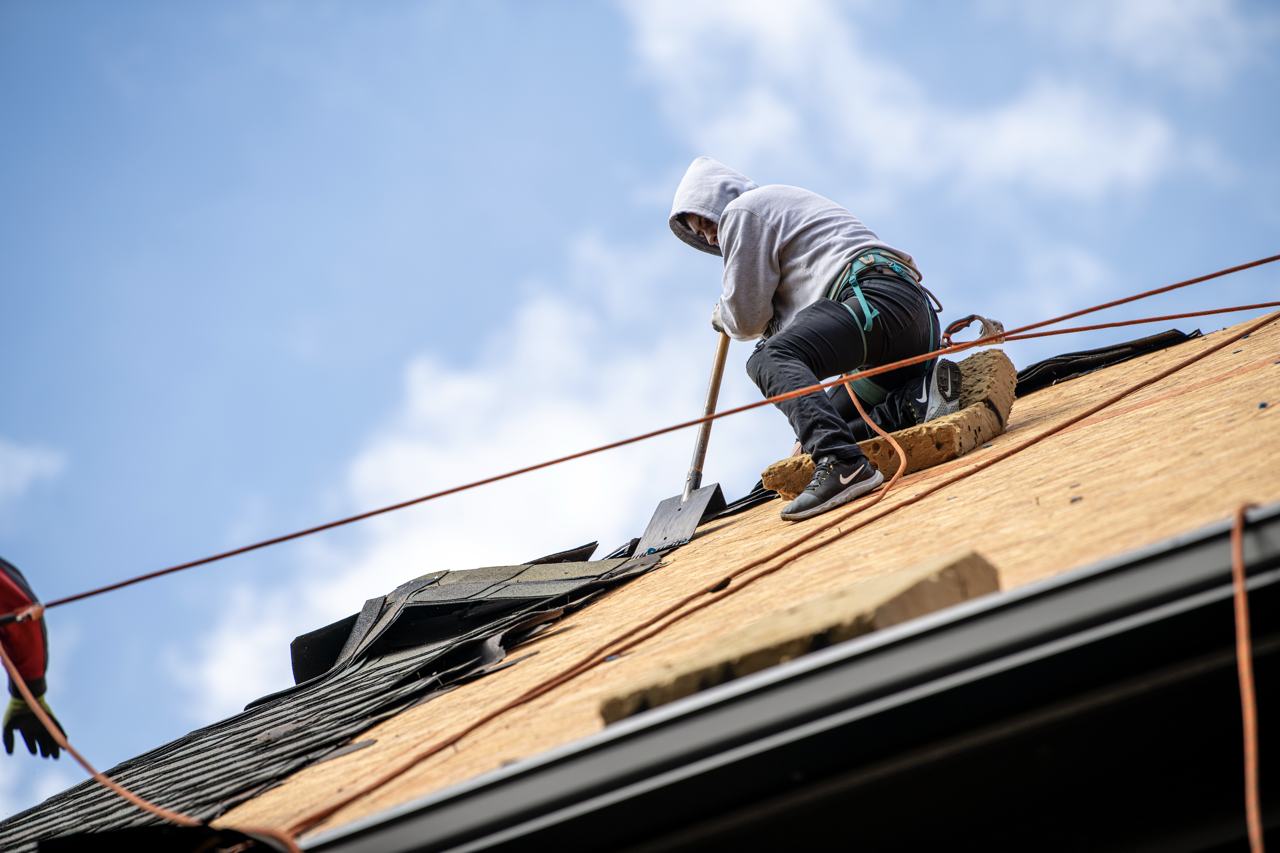 A person climbing on a roof, working on the shingles and roof structure during daylight.