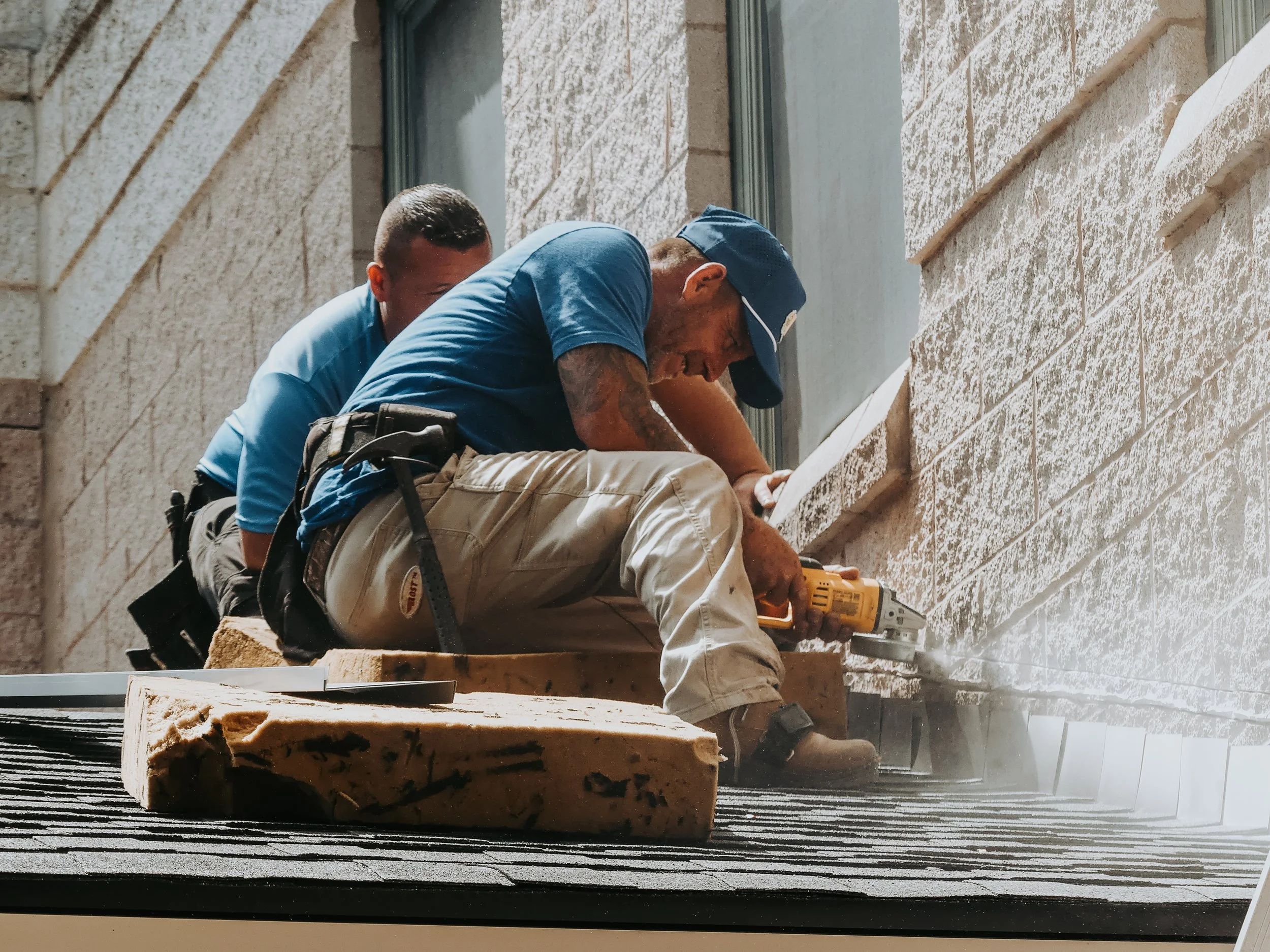 Two construction workers installing brick siding on a building, using a power tool, with insulation foam nearby.