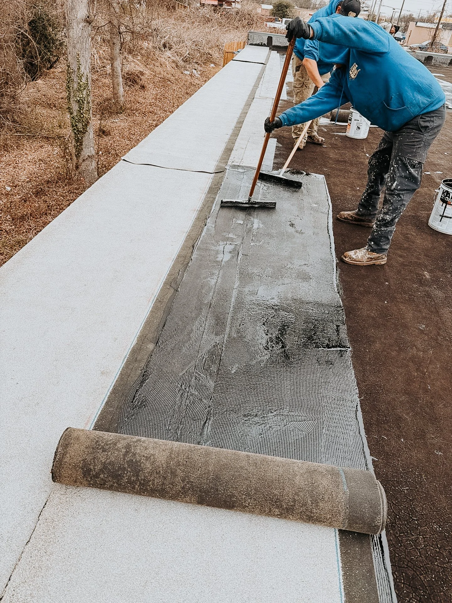 Workers applying a black waterproofing membrane on a flat roof.