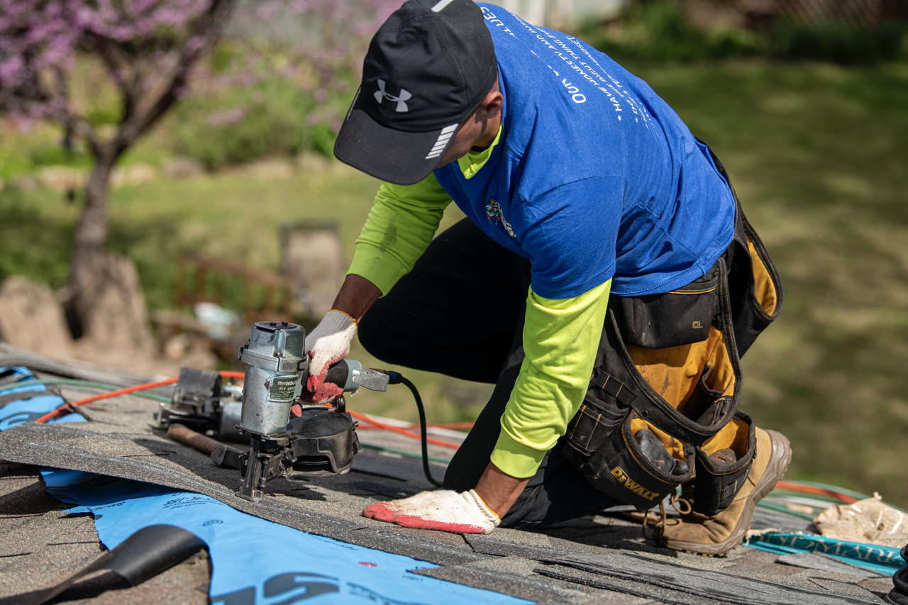 A worker installing or repairing roofing shingles on a roof, using a nail gun.