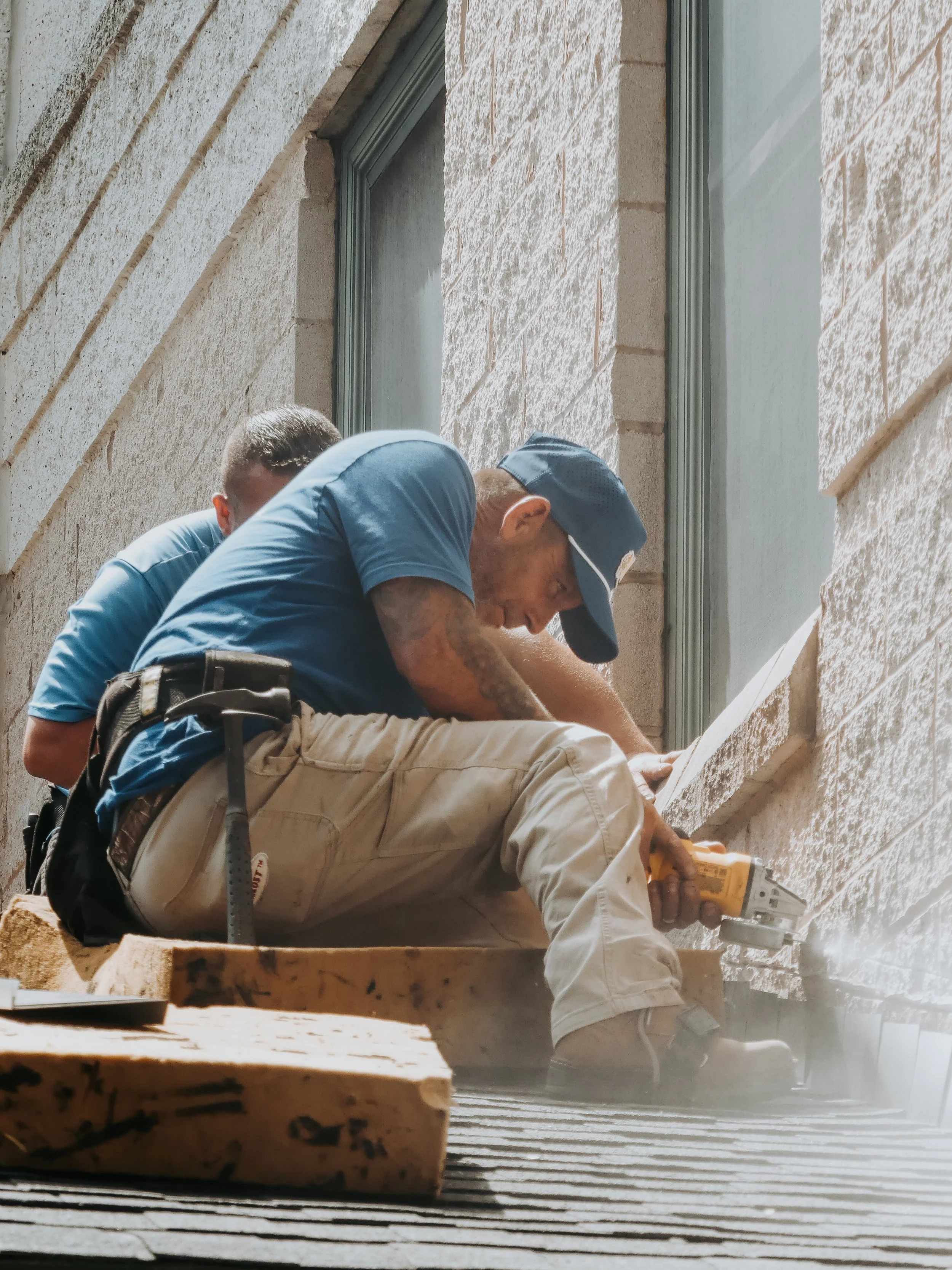 Two construction workers on a scaffold working on a building's exterior wall with tools.