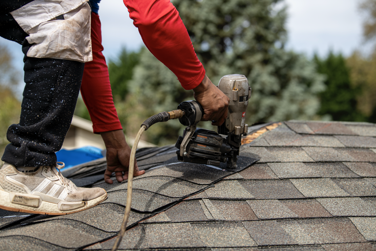 Person working on a roof using a nail gun to attach shingles.
