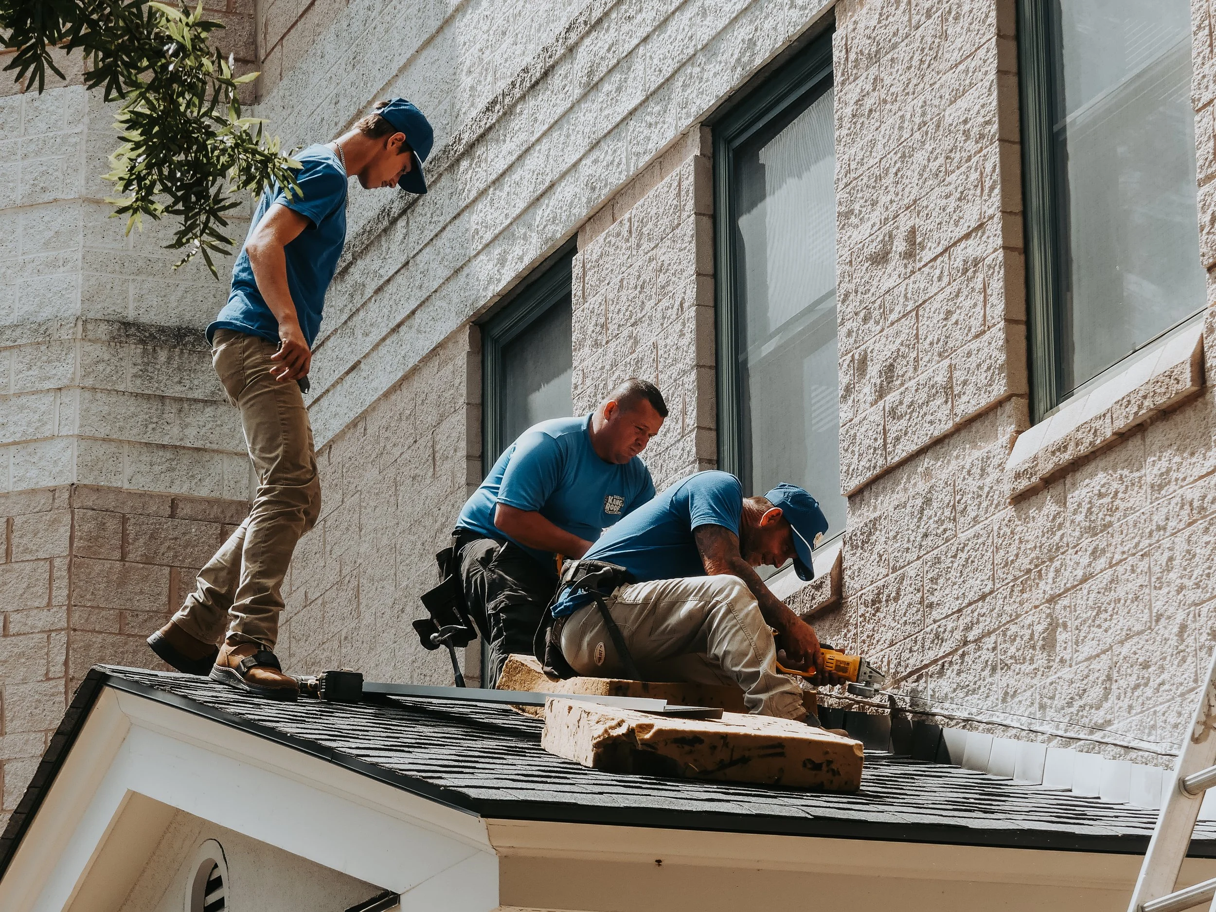 Three workers repairing the exterior window trim on a house, standing and kneeling on the roof.