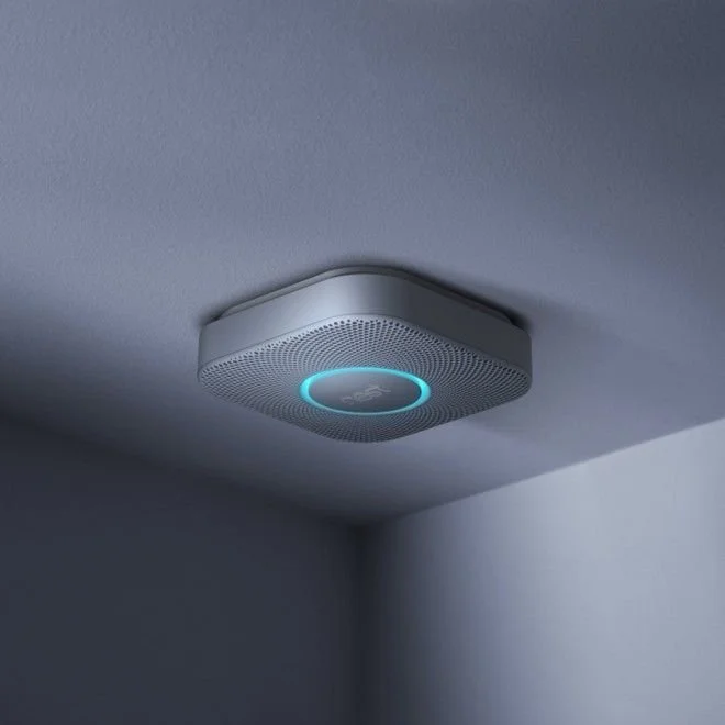 Smoke detector with a blue LED ring on a white ceiling.