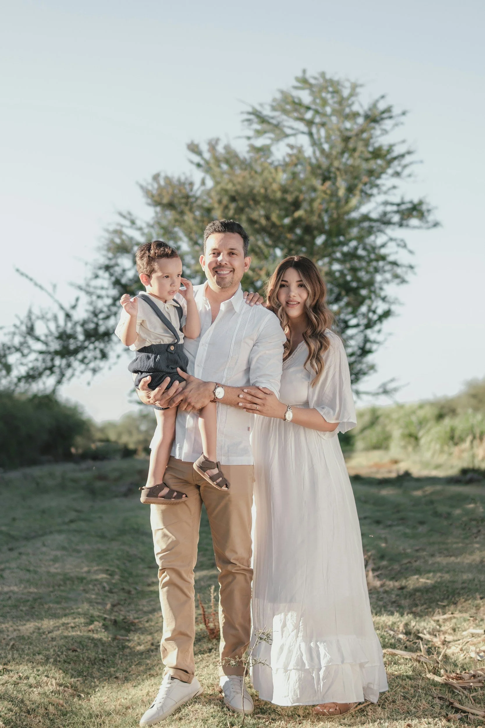 Parents standing together outdoors with their young child during a natural family portrait session.