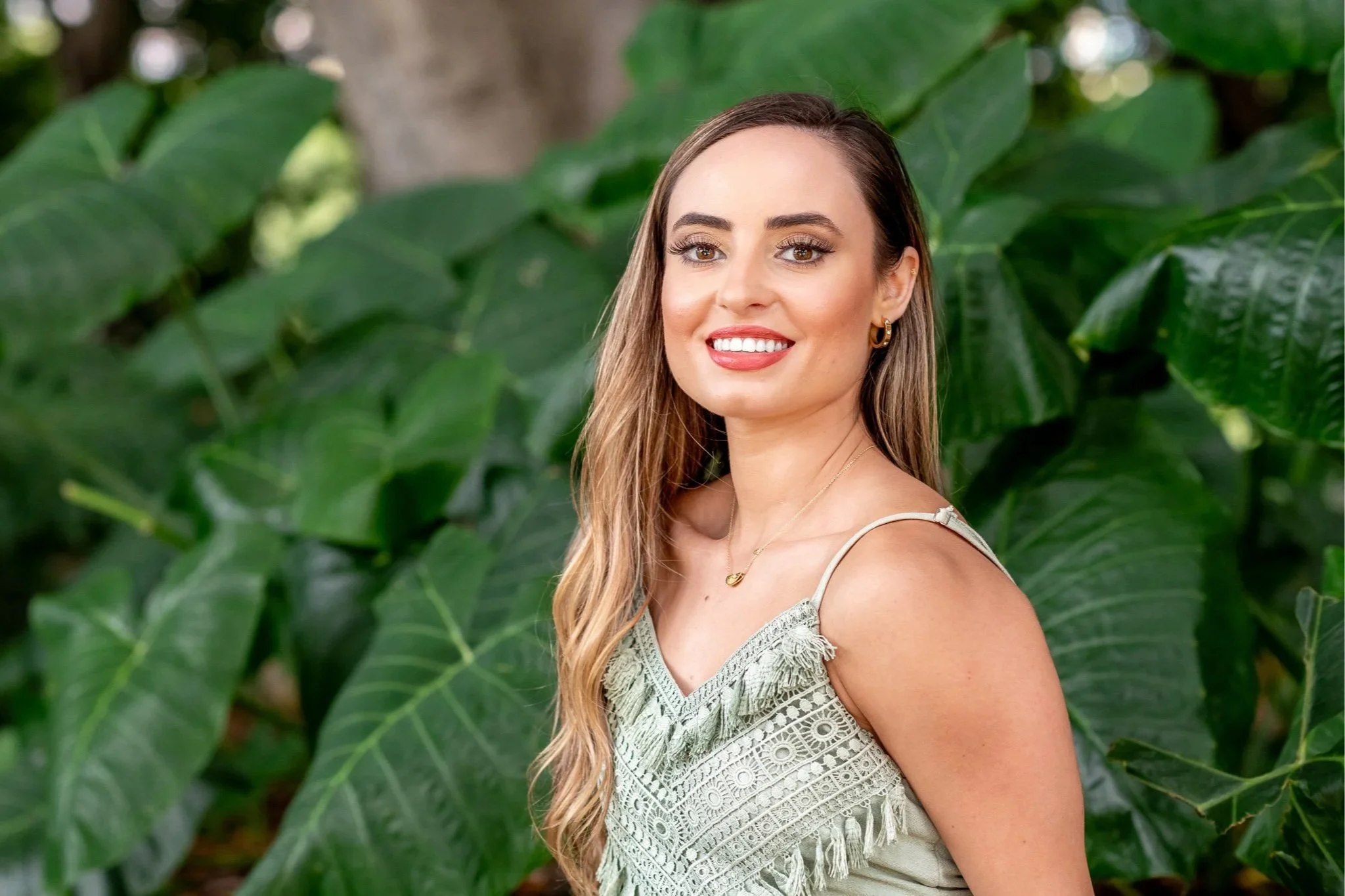 Woman smiling during an outdoor lifestyle portrait session with large green leaves in the background.