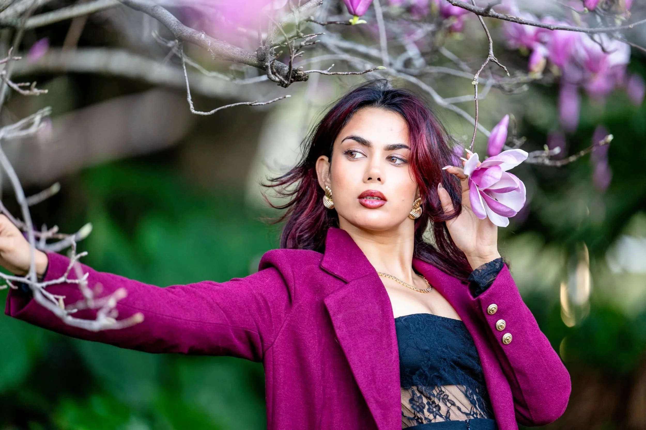 Woman posing for an outdoor lifestyle portrait beside a flowering tree with a softly blurred garden background.