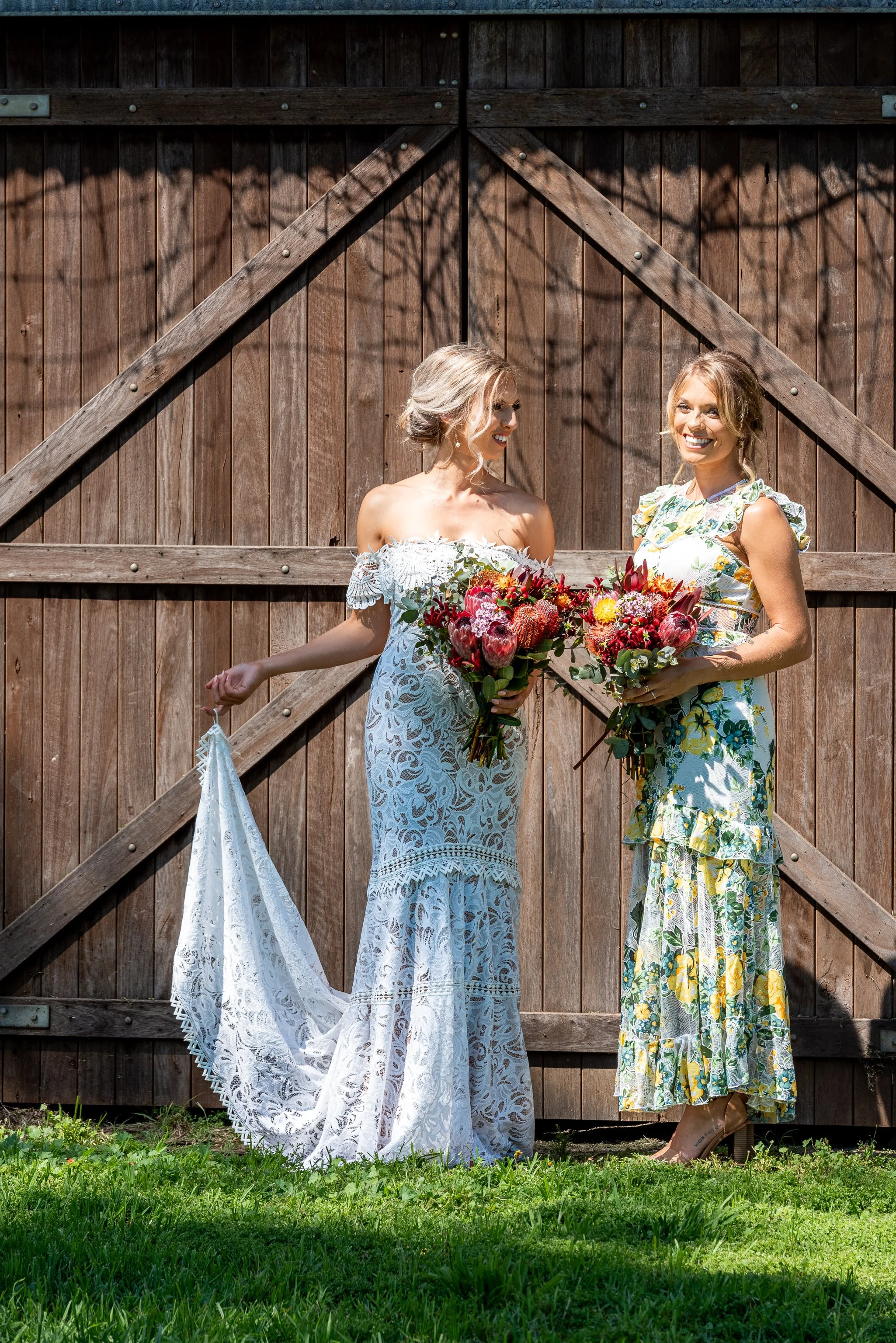 Bride and bridesmaid holding native flower bouquets during an outdoor wedding portrait in front of timber doors.
