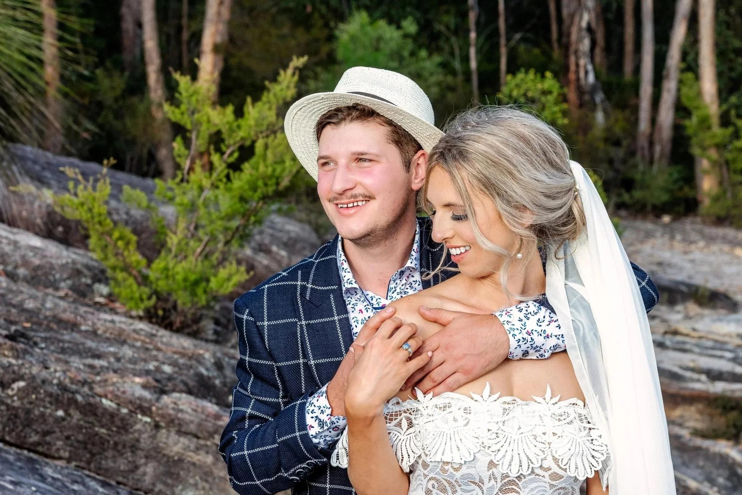 Bride and groom sharing a relaxed outdoor wedding portrait, with the groom embracing the bride from behind.