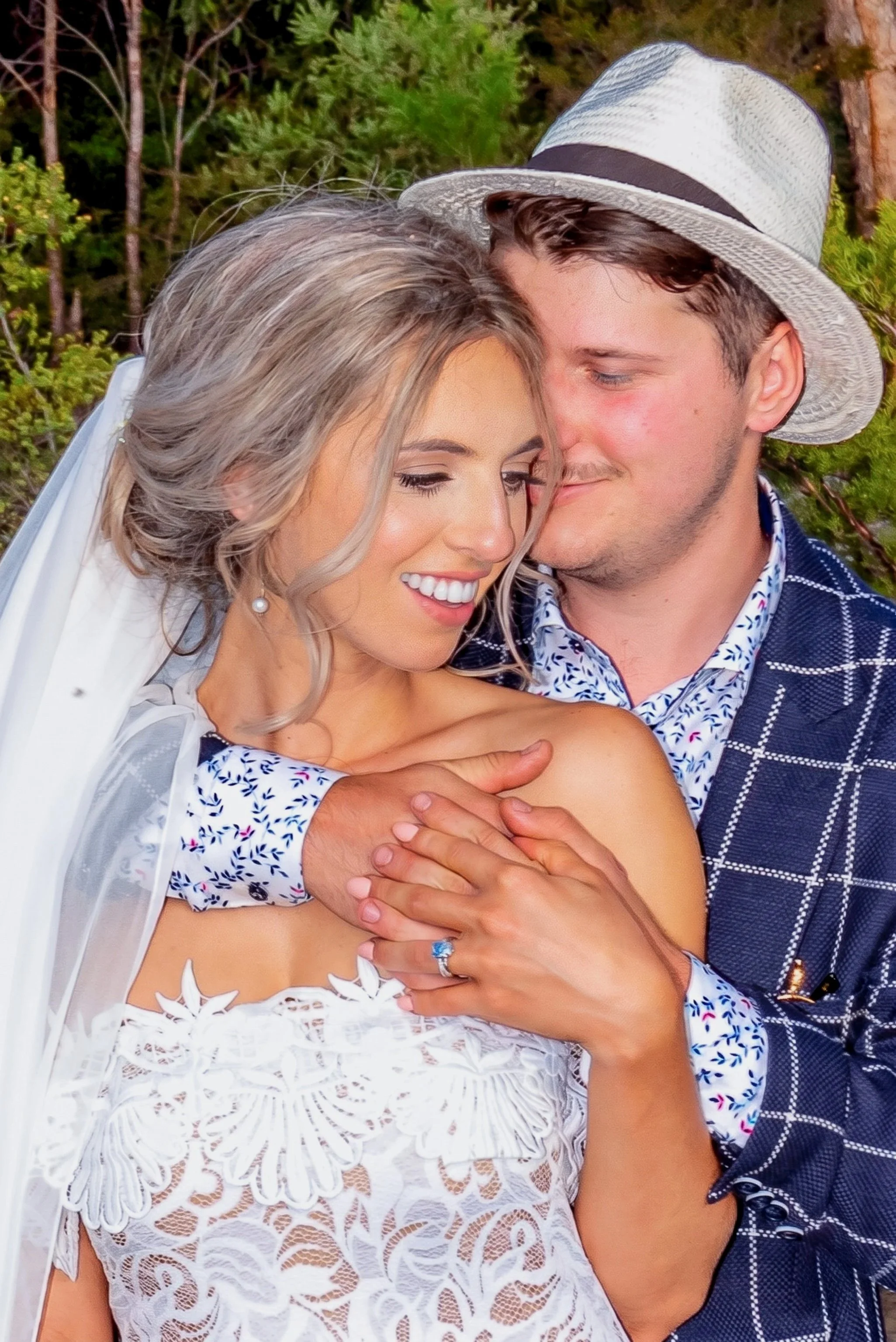 Bride and groom sharing a close outdoor wedding portrait, with the groom embracing the bride from behind.