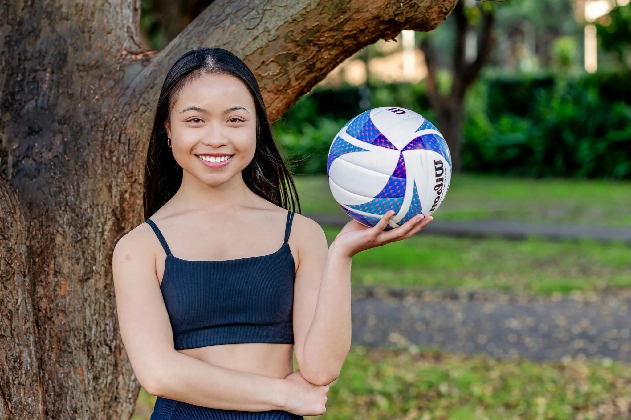 Young athlete holding a volleyball during an outdoor portrait session in a park.