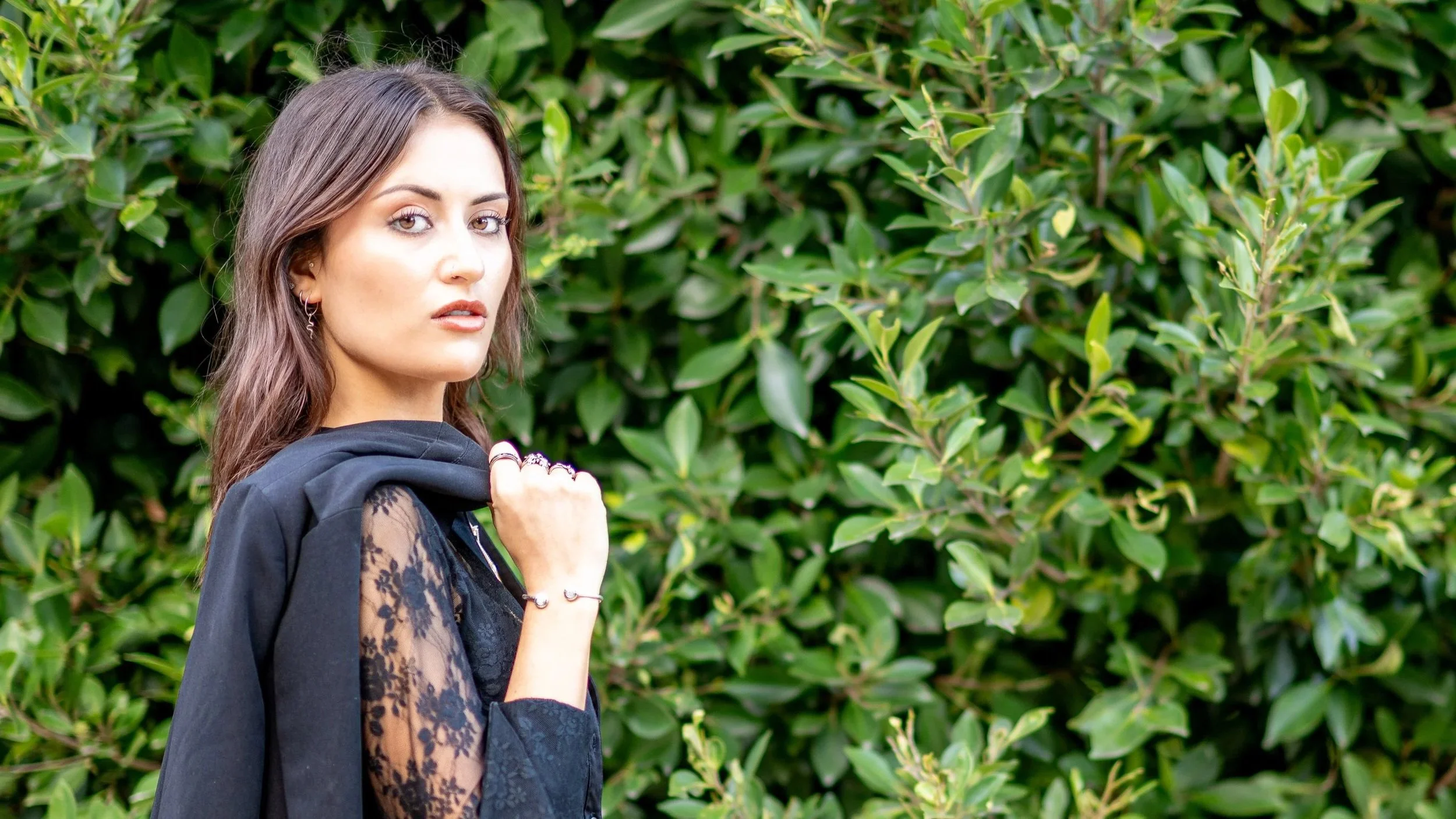 Woman posing for an outdoor lifestyle portrait against a green leafy background.