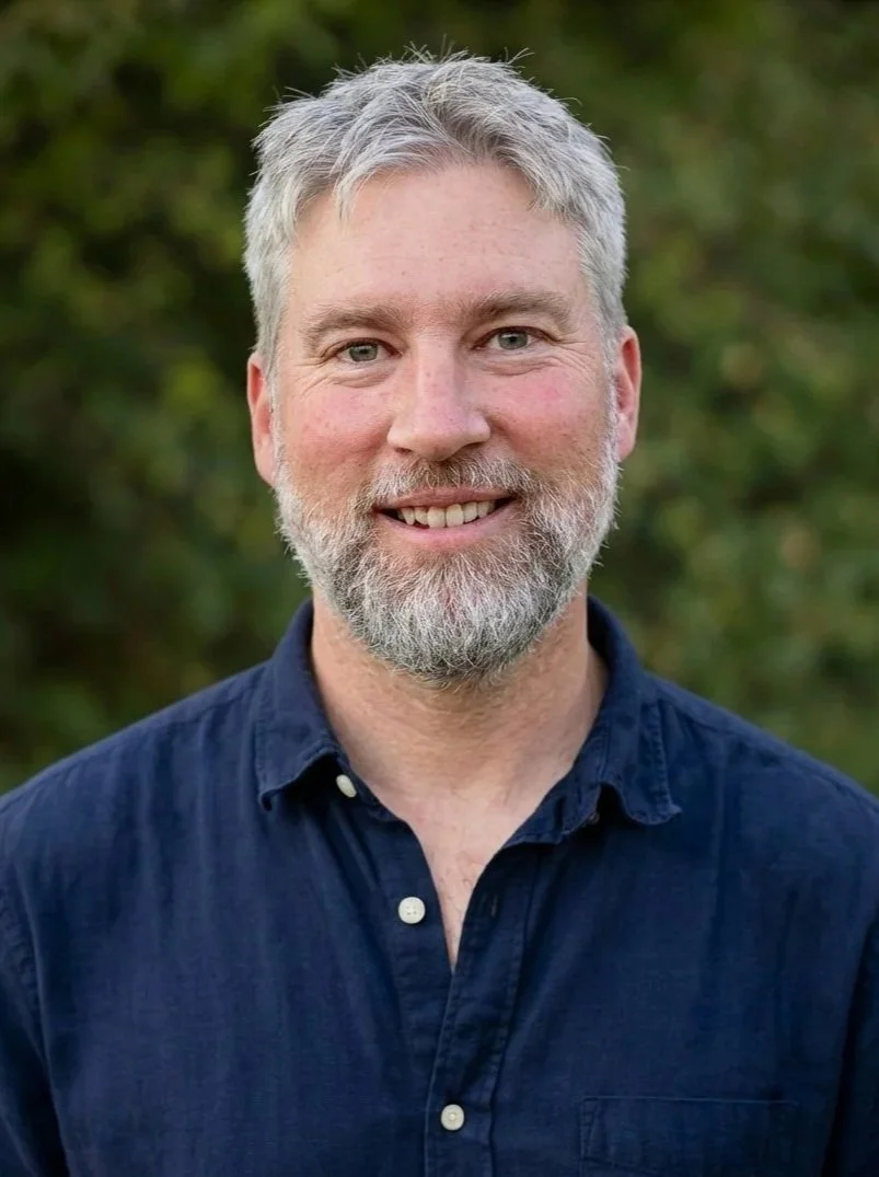 Portrait of Clinton, the photographer behind Water Cloud Images, standing outdoors against a green natural background.