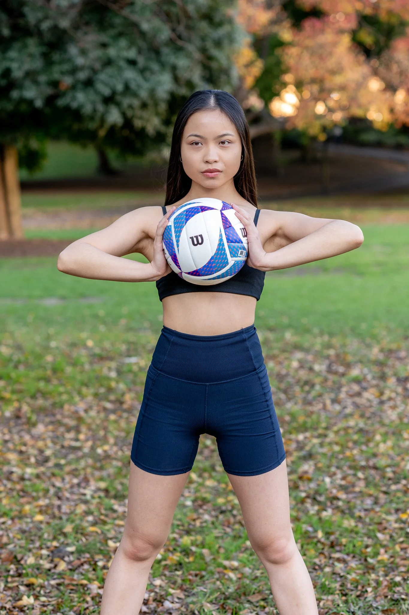 Young athlete holding a volleyball during an outdoor portrait session in a park.