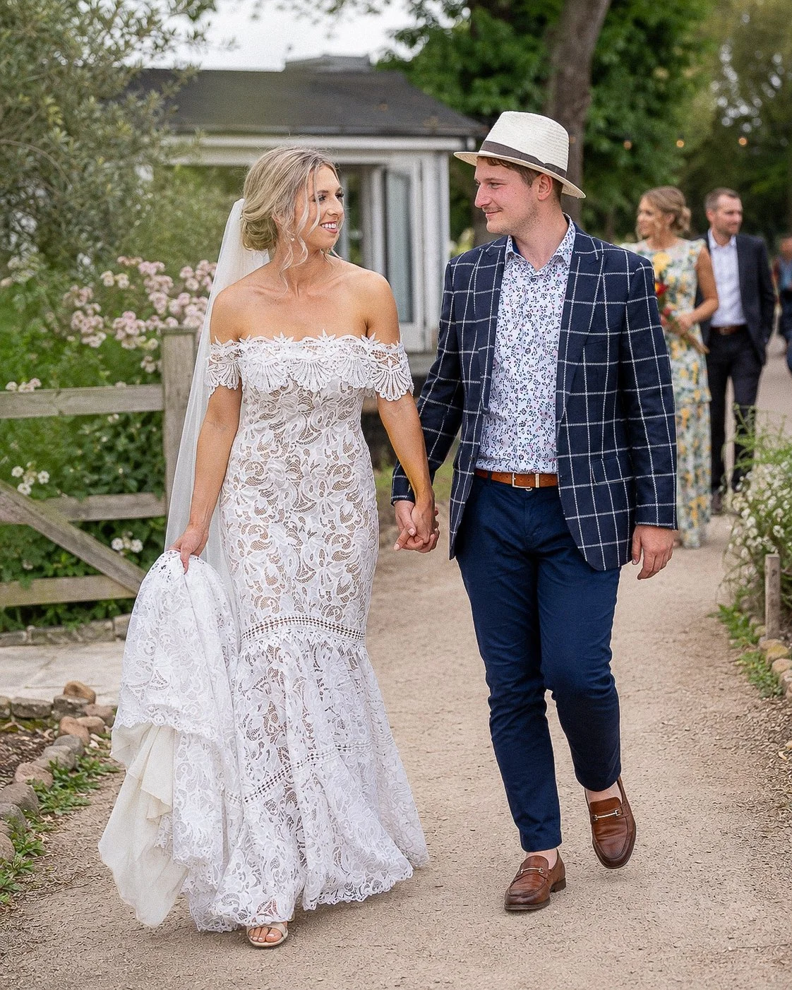 Bride and groom walking hand in hand along a garden path.