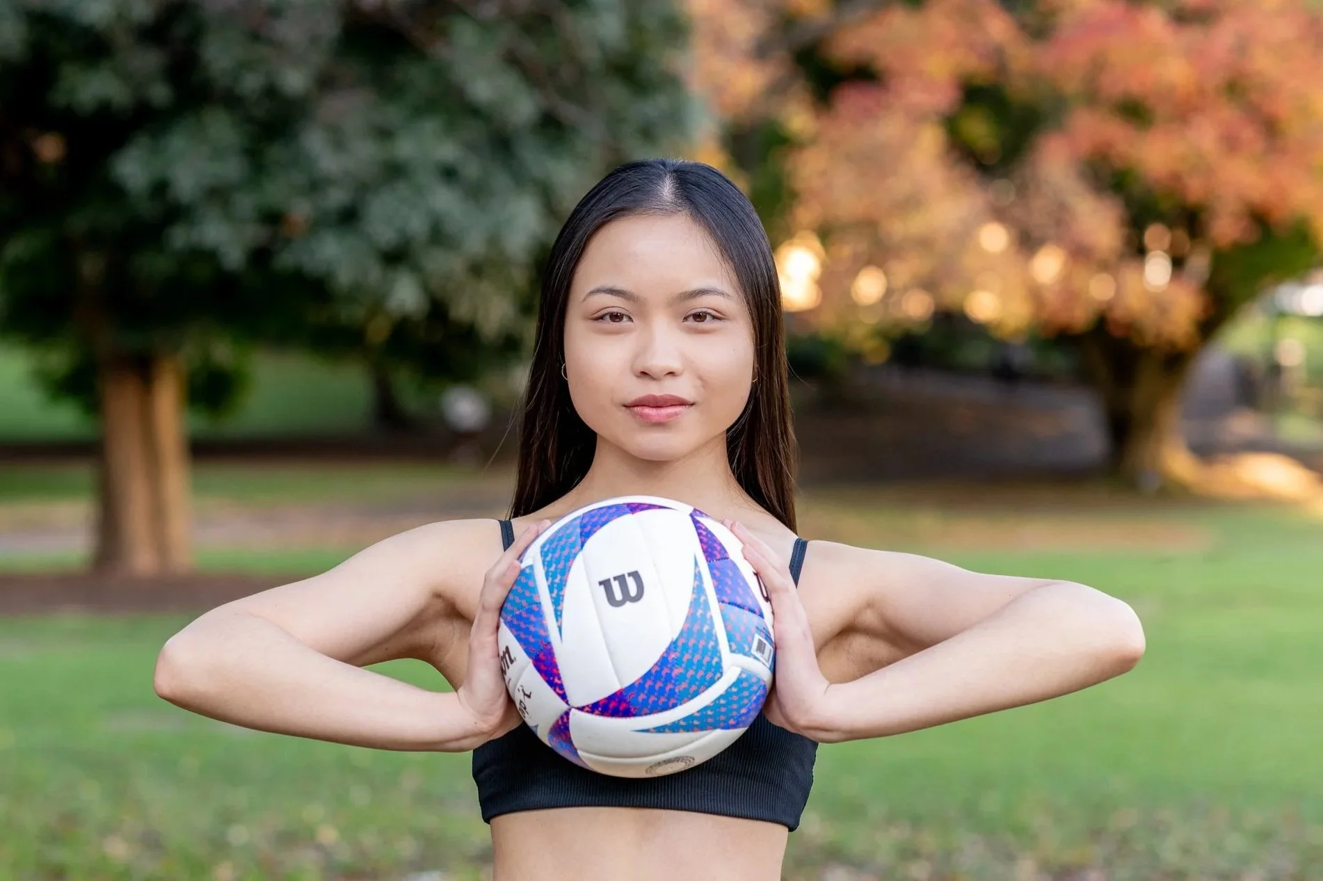 Young woman holding a volleyball during an outdoor portrait session in a park.