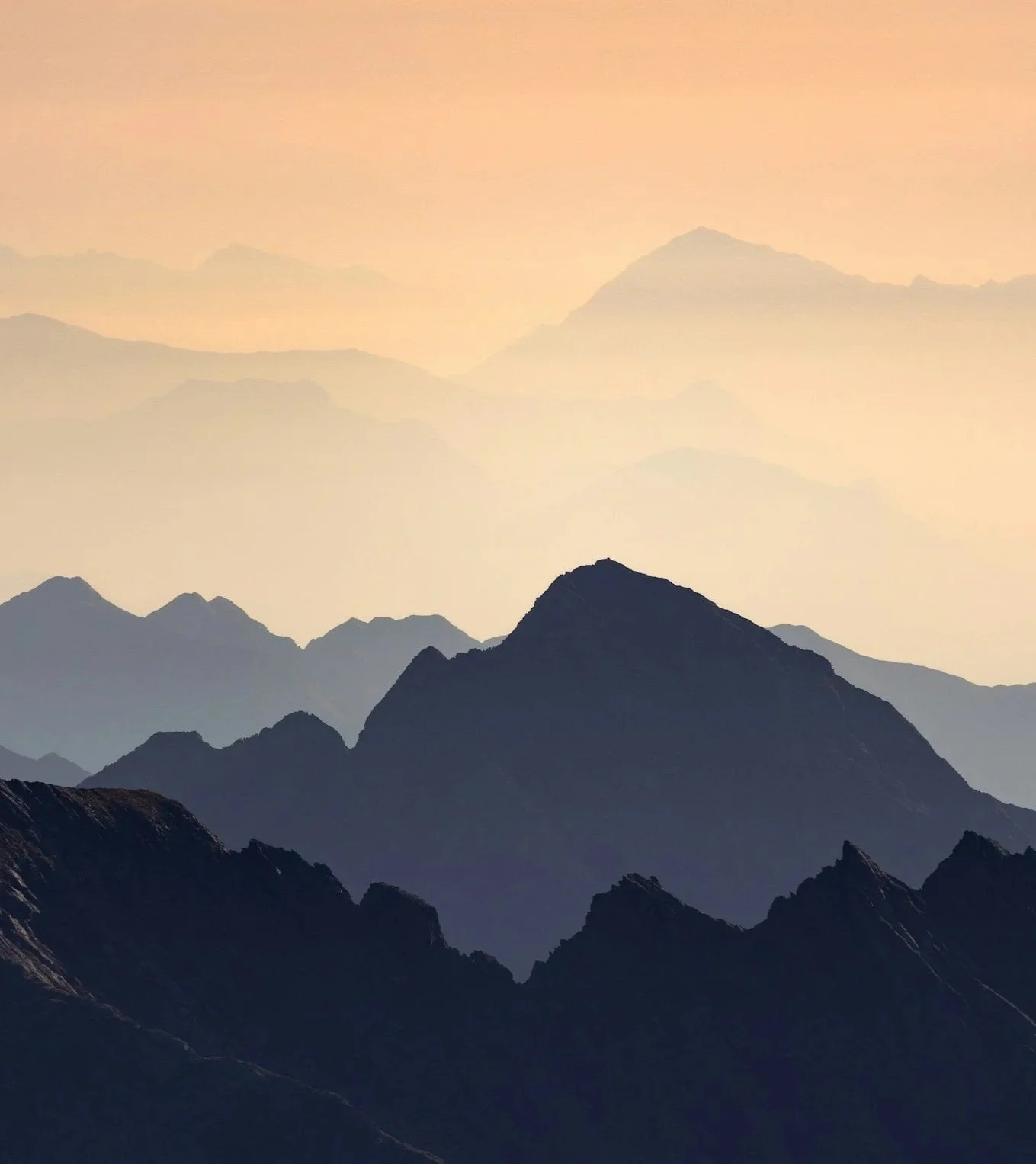 A scenic view of multiple mountain ranges at sunset with a gradient sky.