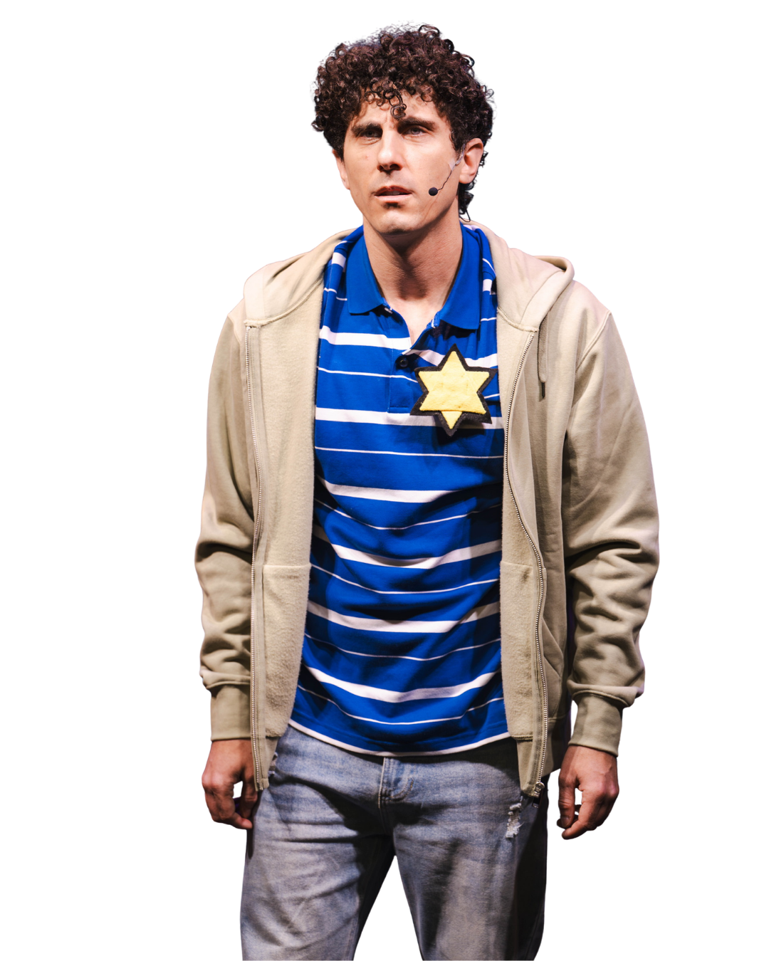 A man with curly hair wearing a blue and white striped polo shirt, a beige zip-up hoodie, and a star-shaped badge, standing with a serious expression.
