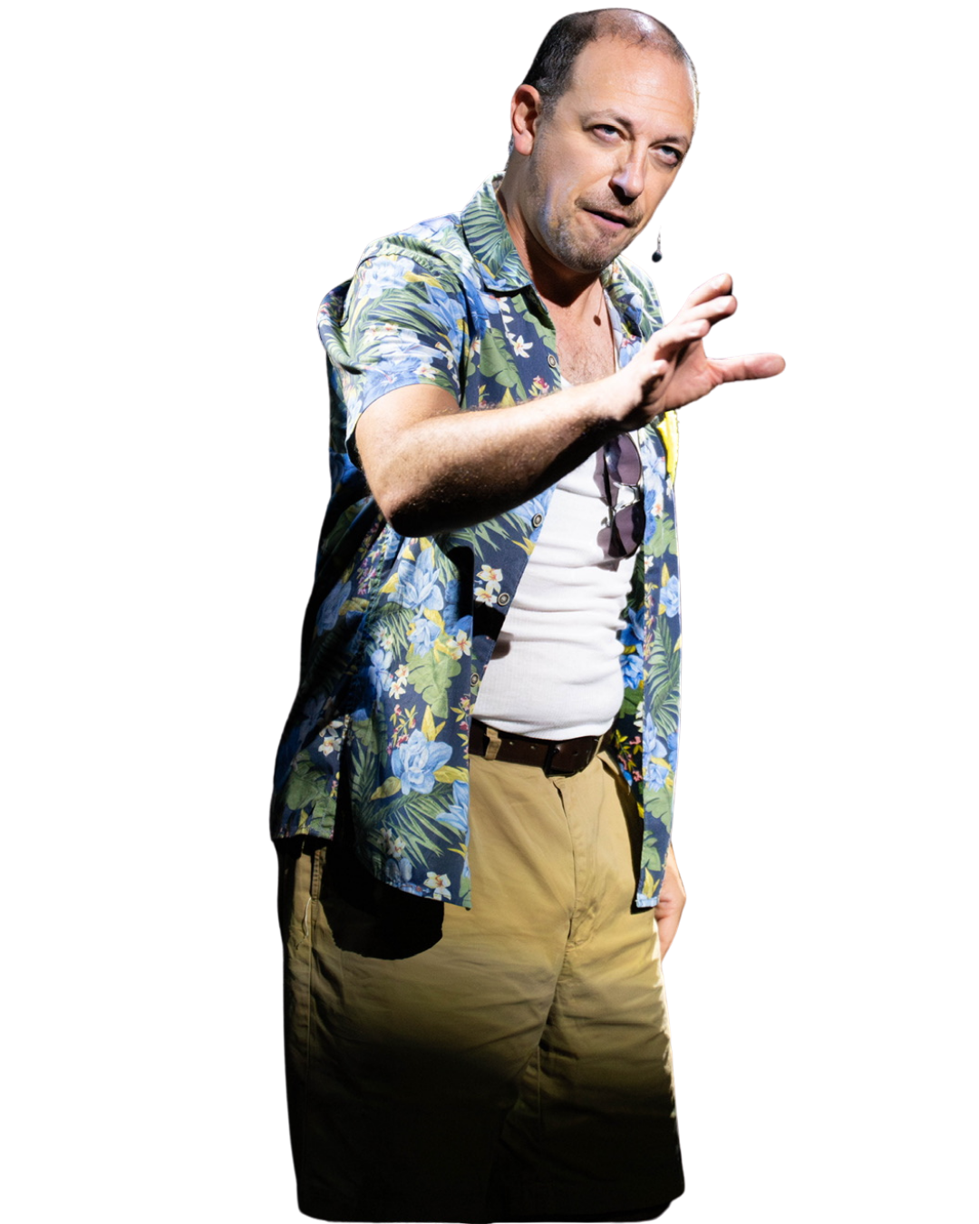 A man with short dark hair, a beard, and light complexion, wearing a matching white T-shirt and beige pants, with sunglasses hanging from his shirt collar, and a blue floral short-sleeve shirt over it, making a gesture with his right hand, against a black background.
