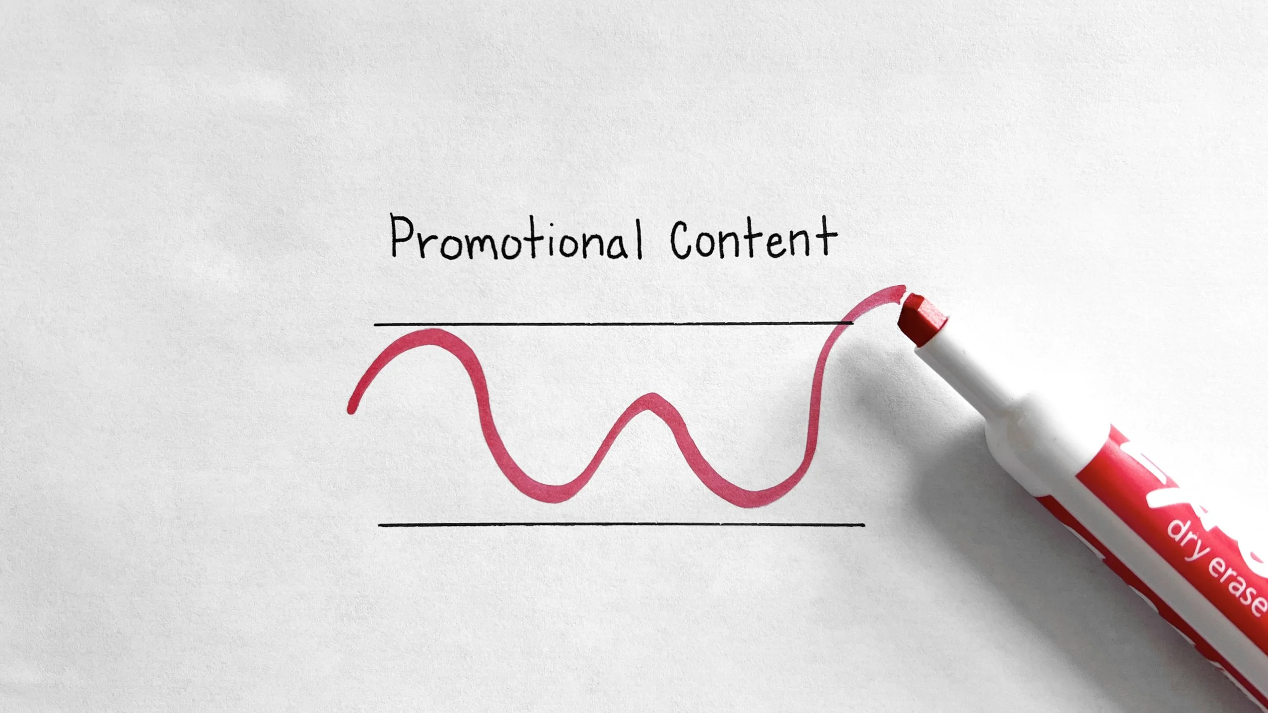A white surface with handwritten words 'Promotional Content' and a pink line graph beneath it, with a red and white dry erase marker placed on the right side.