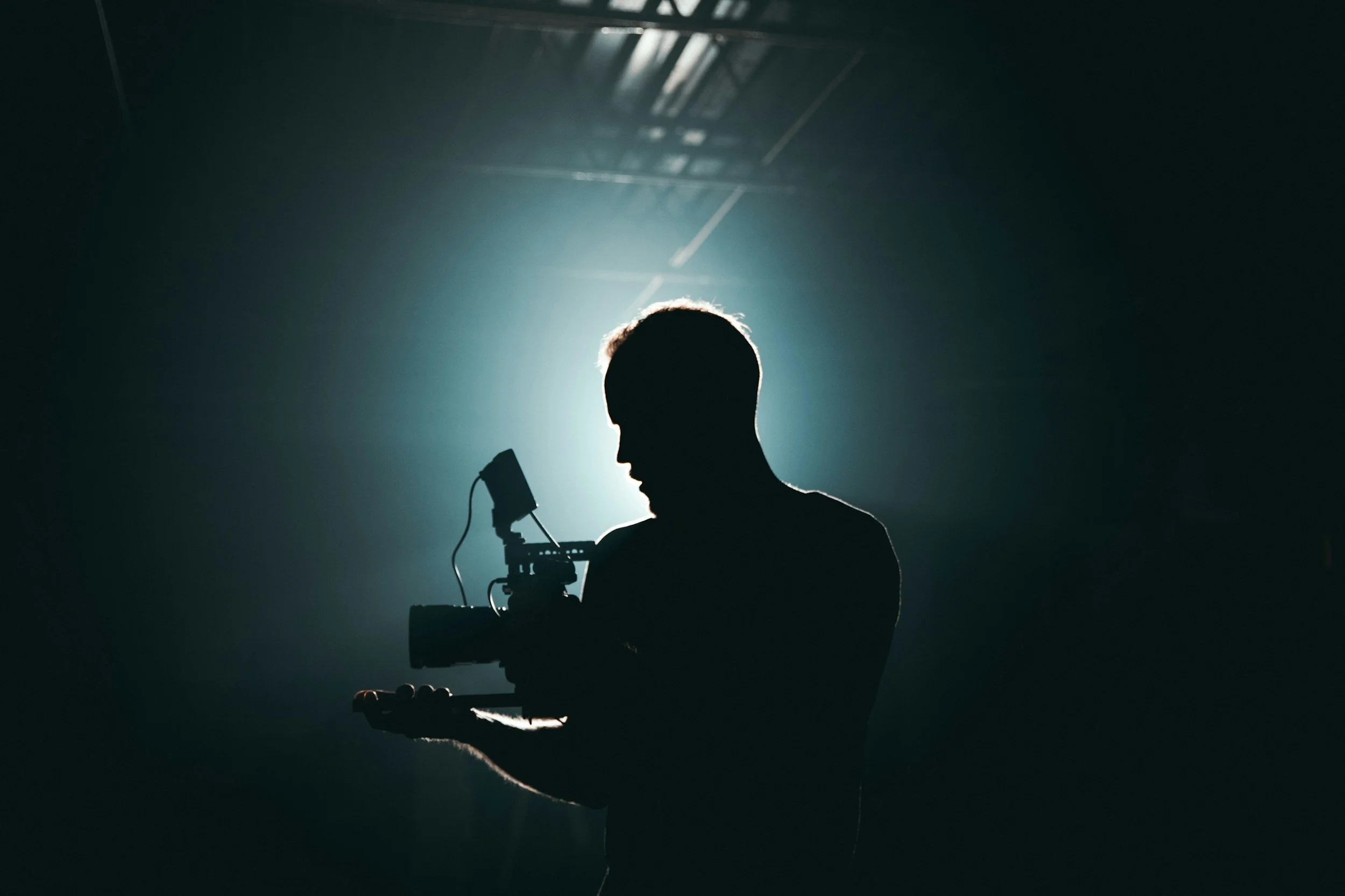 Silhouette of a person holding a camera or filming equipment against a bright light background.