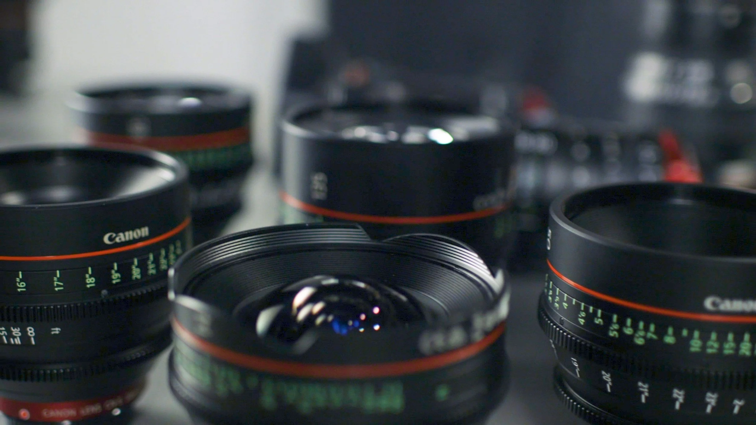 Close-up of several Canon camera lenses with black bodies and calibration markings, arranged on a surface.