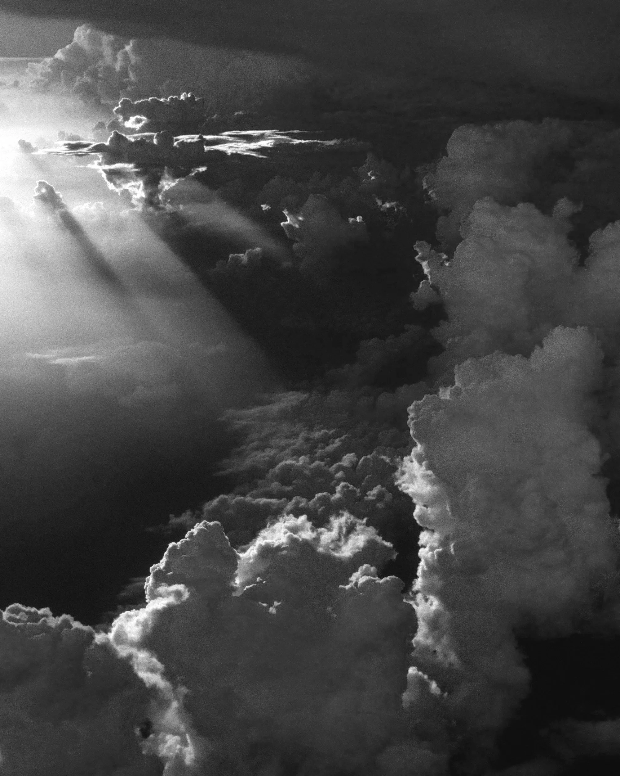A sky filled with large, dark, and dense clouds, with sunlight piercing through and illuminating parts of the cloud formation, creating rays of light.